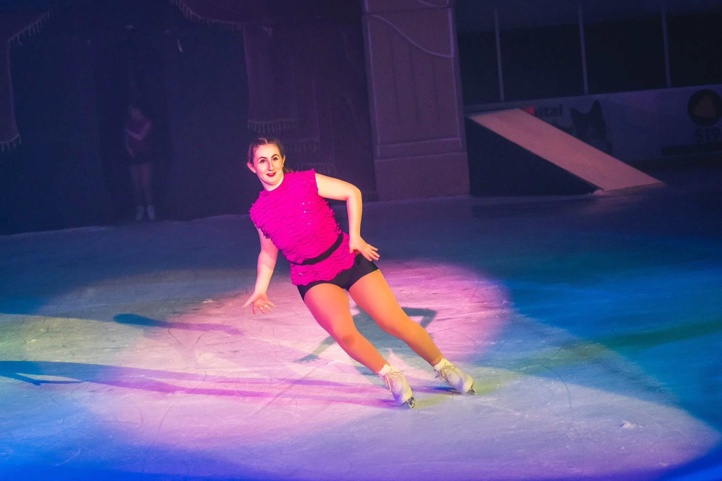 A young female figure skater in a pink dress gliding on ice skates during a performance or practice session.