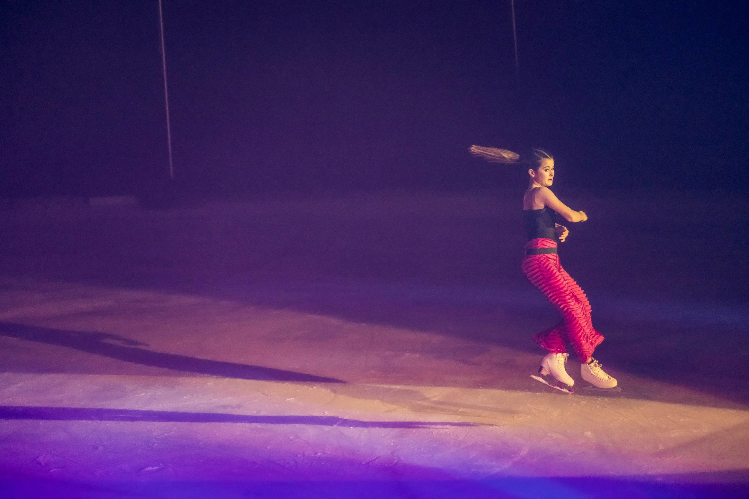 A woman spinning on ice skates in a dark, indoor ice rink with colorful lighting.