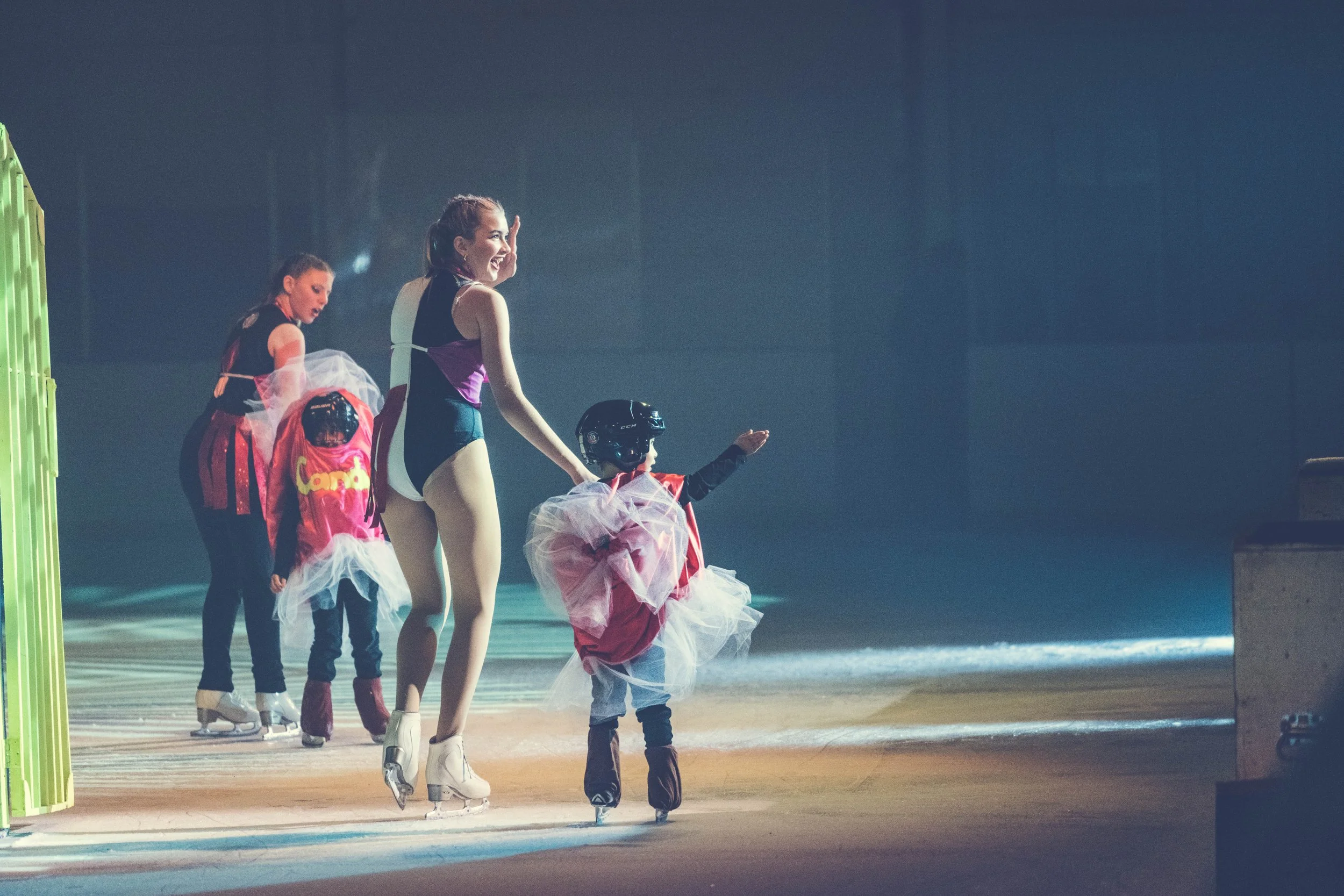 Children and a figure skater in an ice skating rink, with some children dressed in costumes and a woman in figure skating attire.