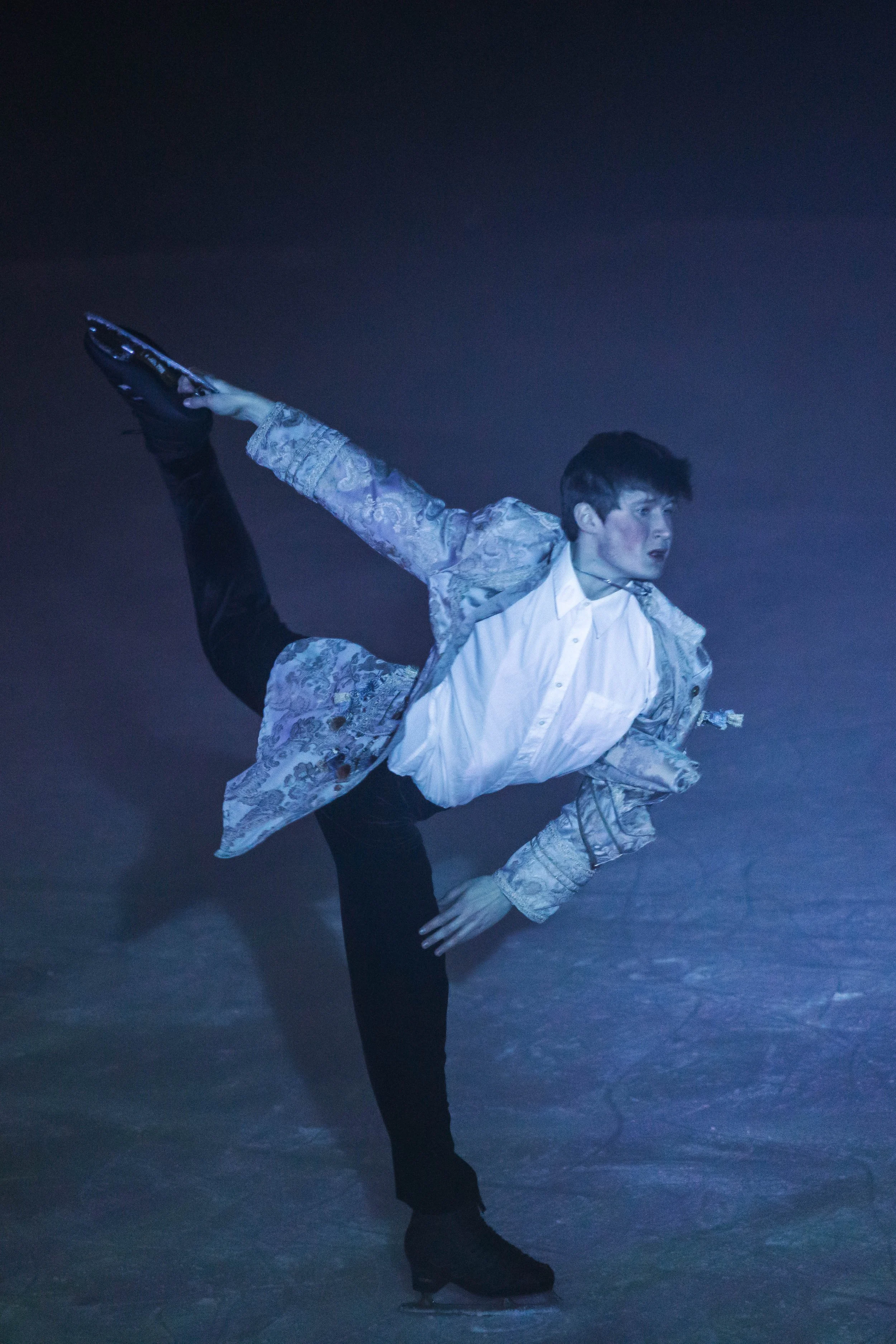 Ice skaters performing a dance routine on the ice in a dark setting.