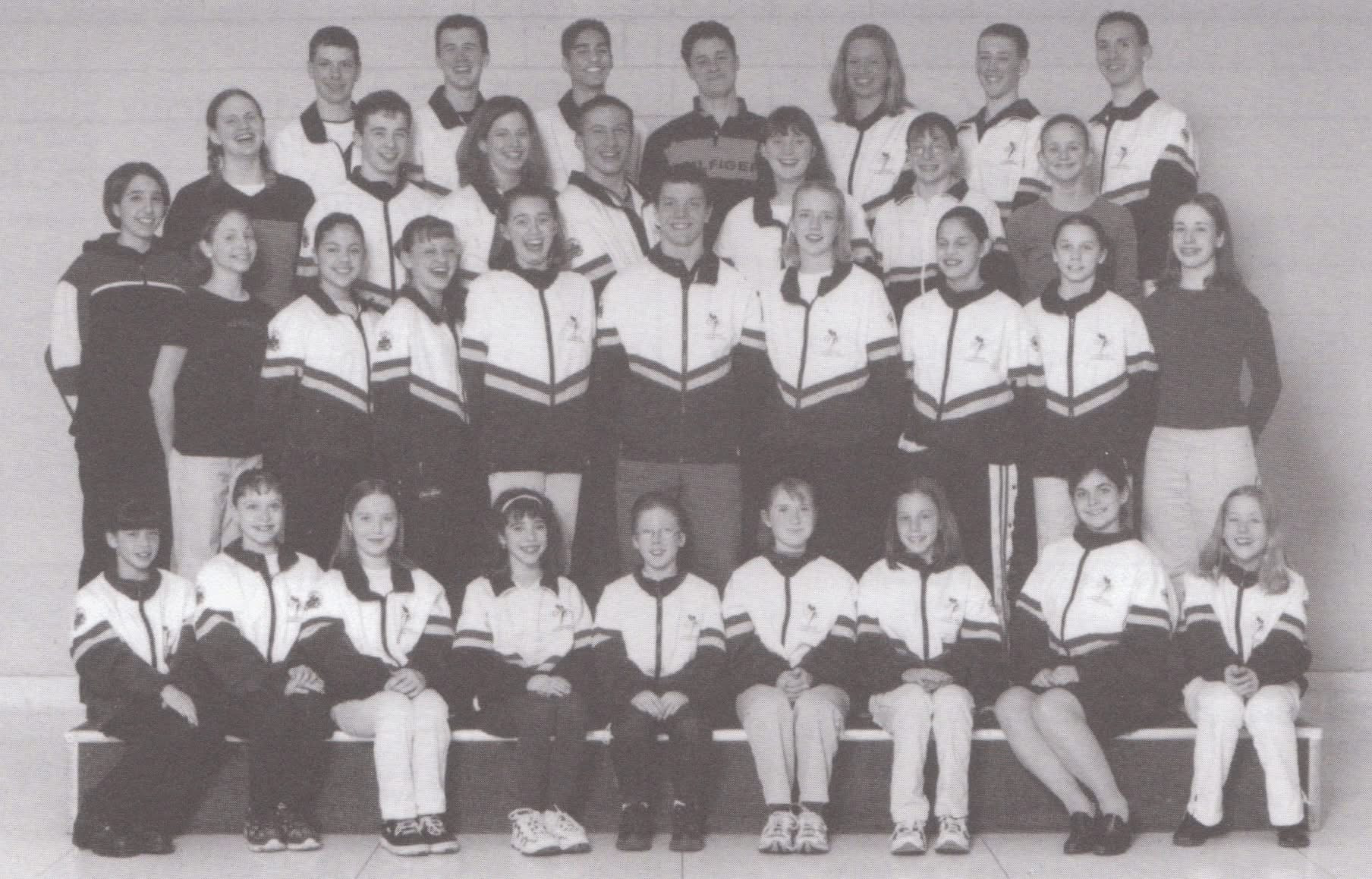 A black-and-white group photo of young athletes and coaches, arranged in rows, wearing sports uniforms, smiling at the camera.