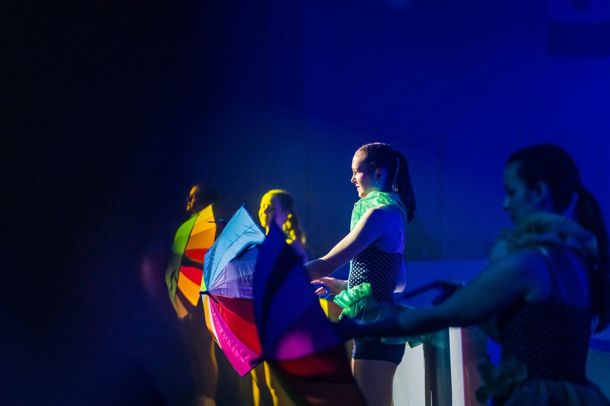 A group of young girls holding colorful kites and standing together, illuminated by blue light in a dark environment.