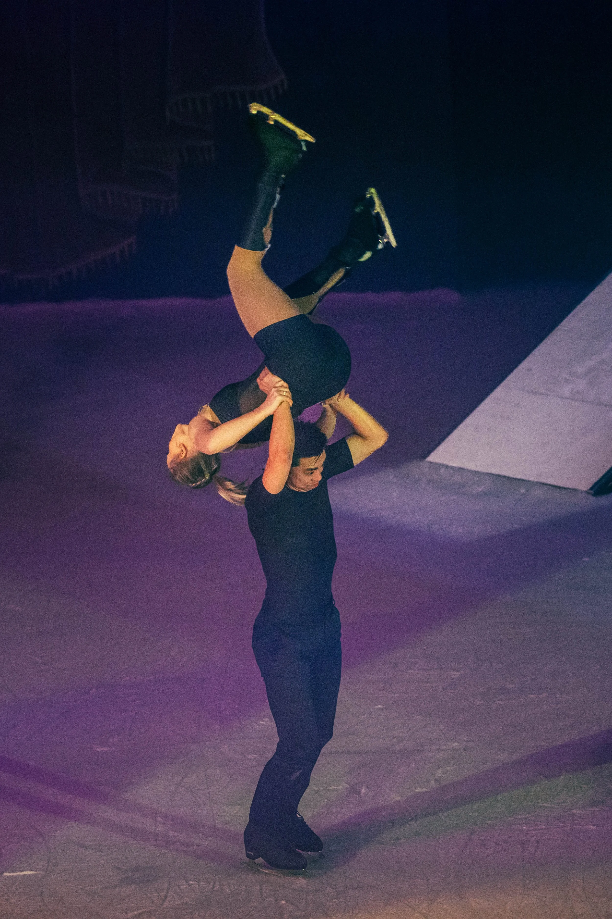 Two women practicing figure skating on an ice rink, with one woman supporting the other in an ice skating pose.