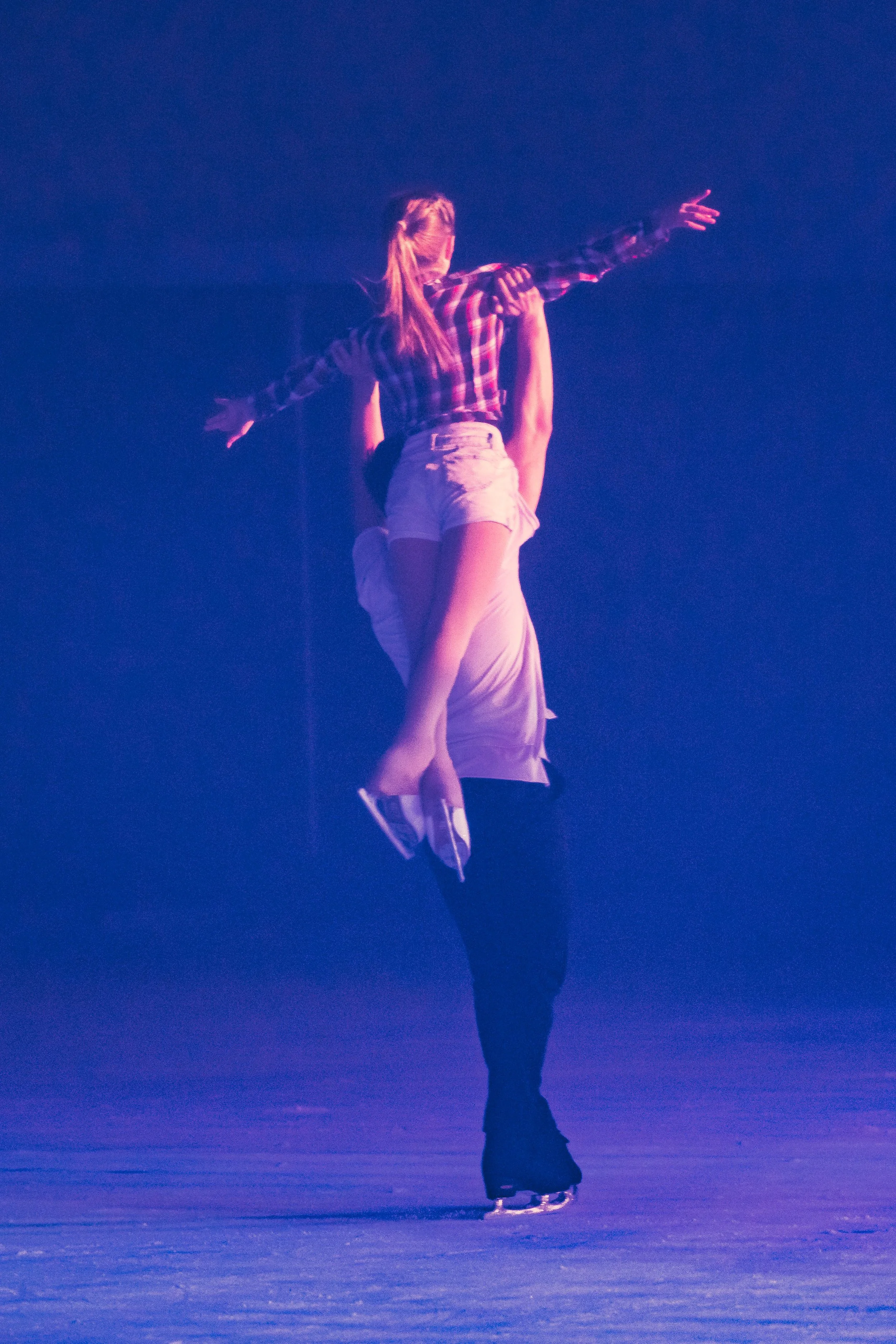 A figure skater performing a spin on ice, with a blue background and purple lighting.