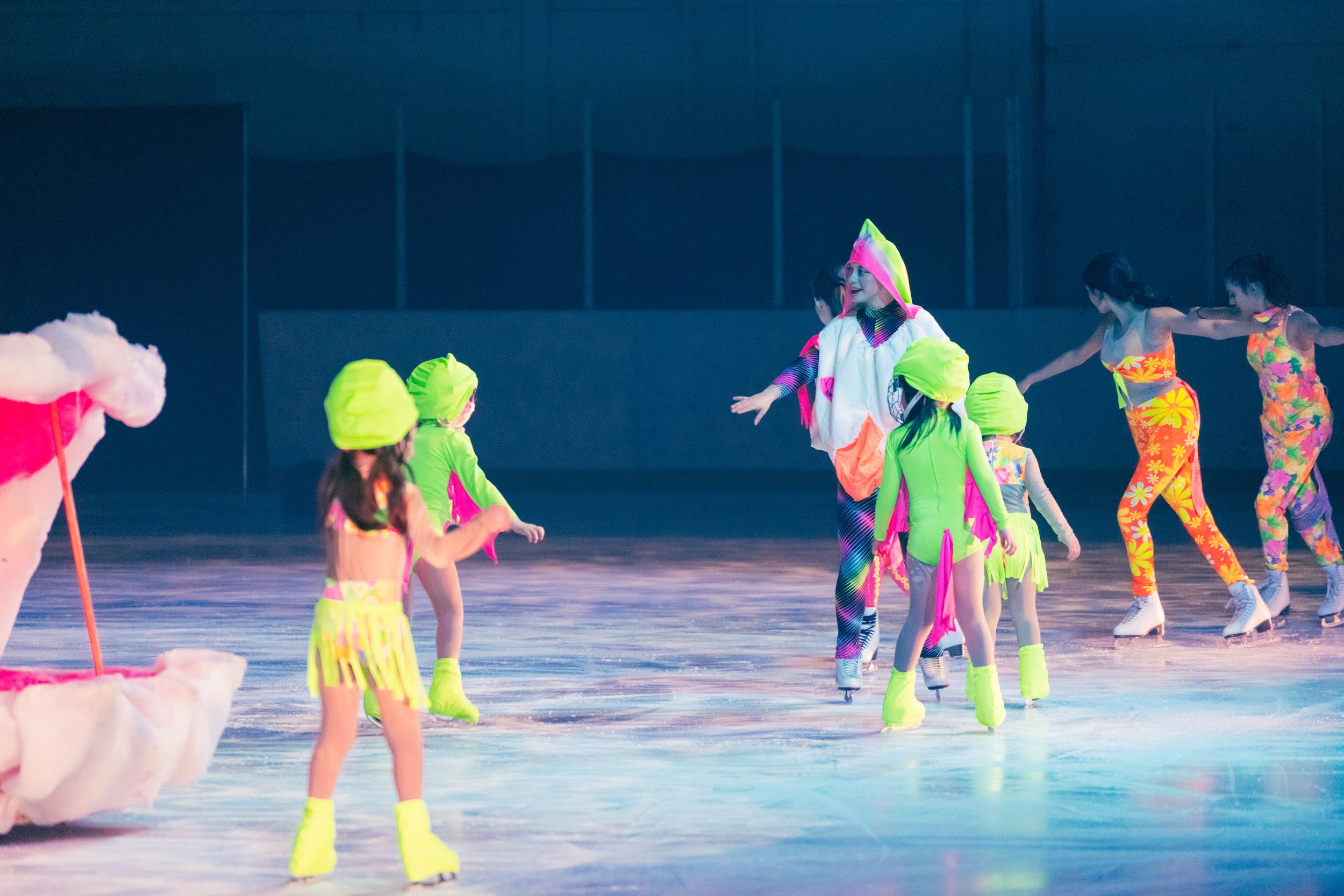 Children in colorful costumes skating on an ice rink, participating in a performance or event.