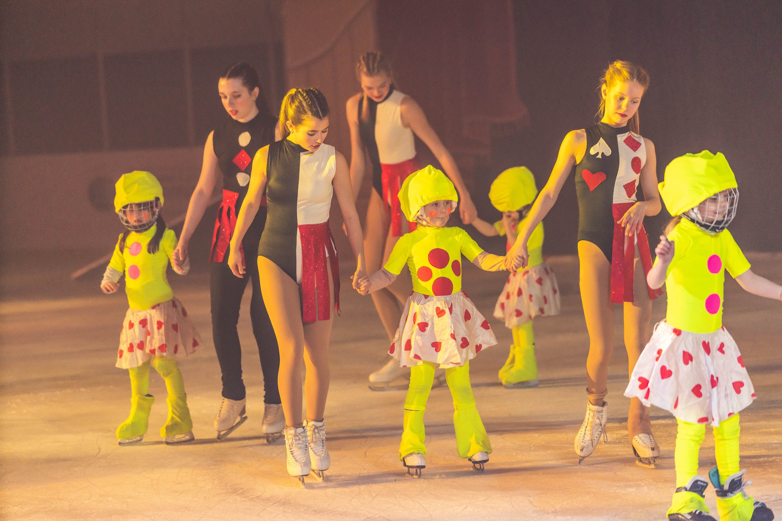 Children wearing colorful costumes ice skating in a line during a performance.