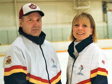 Two people in matching Olympic team jackets standing together at an ice rink