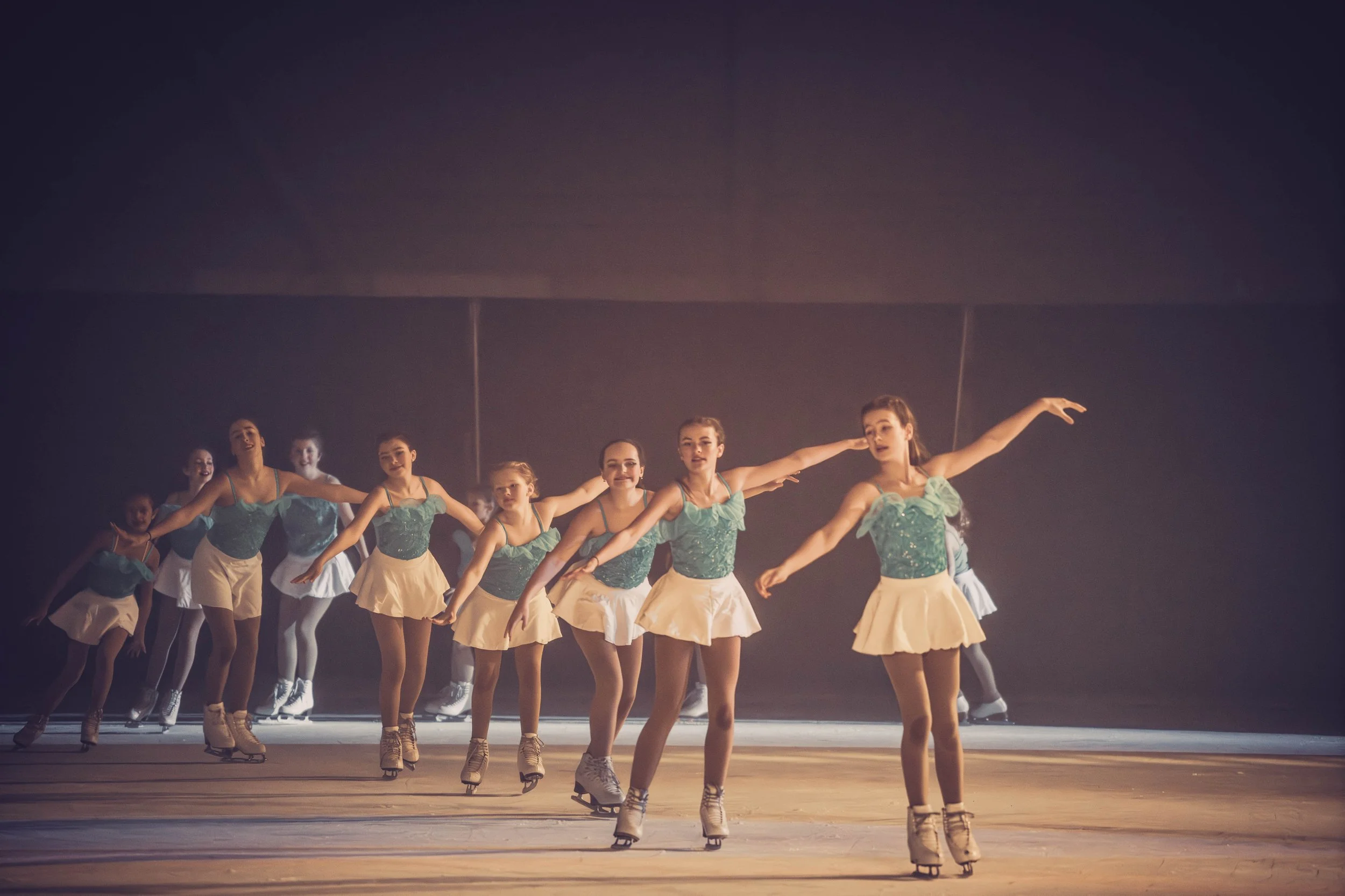 A group of young ballet dancers performing on stage in costumes, with arms extended and poised.