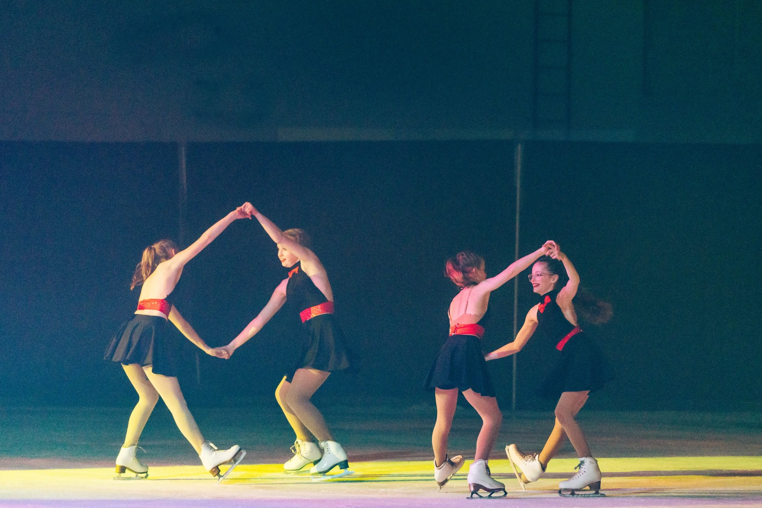 A group of female figure skaters holding hands and performing a synchronized routine on the ice.