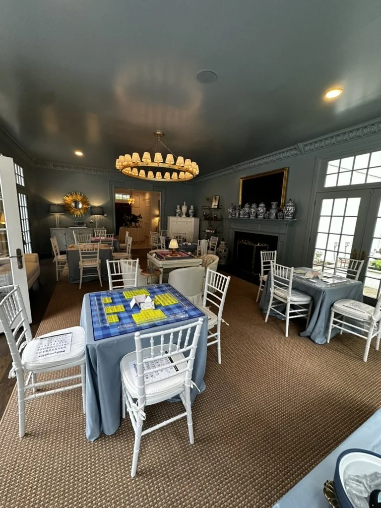 A dining room with multiple tables and chairs, decorated in a classic style with a large chandelier, fireplace, and large windows letting in natural light.