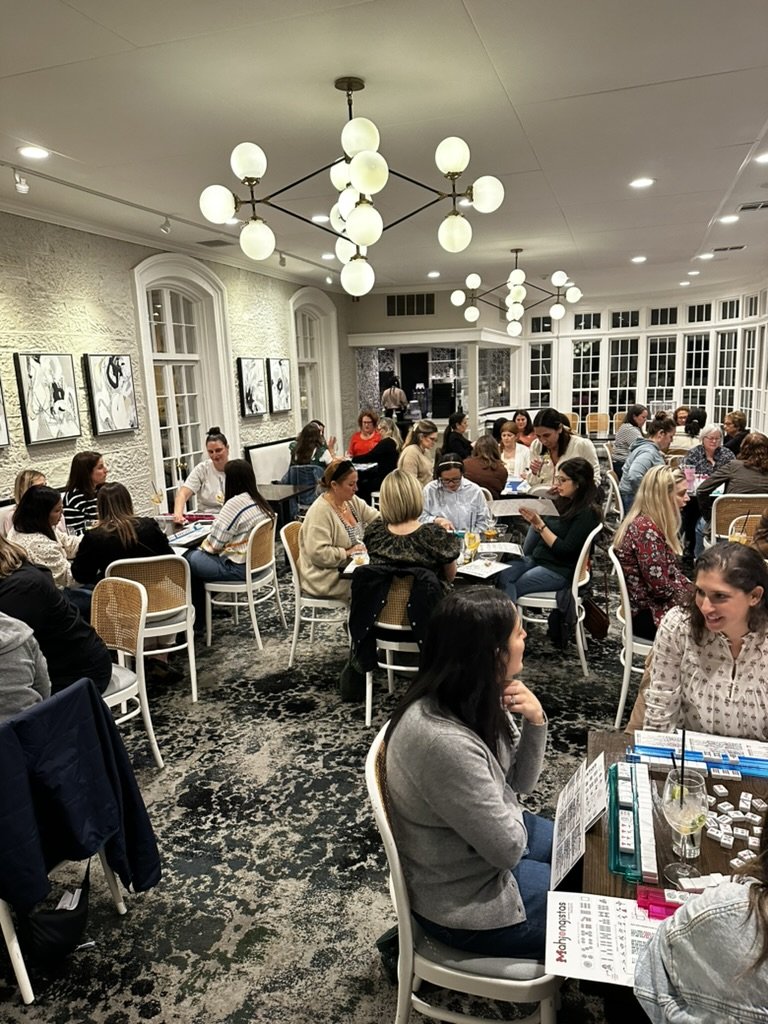 A restaurant filled with women sitting at tables engaged in conversation, with a cozy interior and modern lighting fixtures.