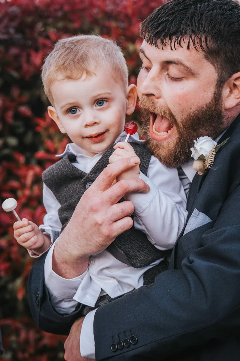 Man and young boy enjoying their time together, holding lollipops, with a background of red autumn leaves.