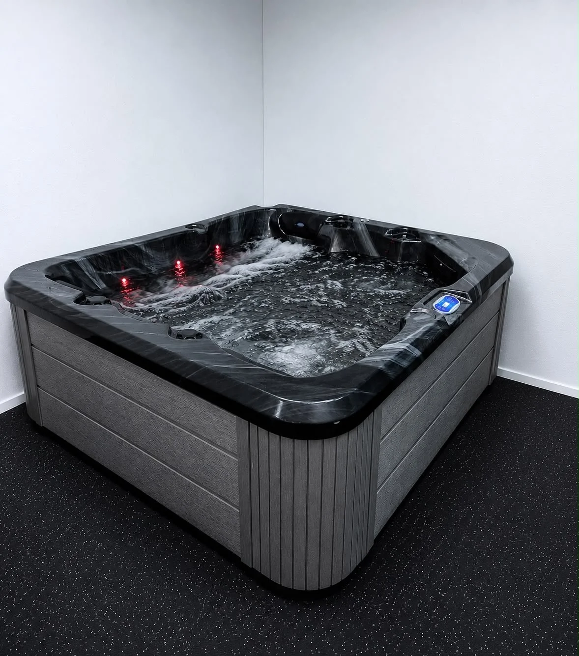 A black hot tub with water jets and a control panel, situated in a white corner of a room with black speckled flooring.