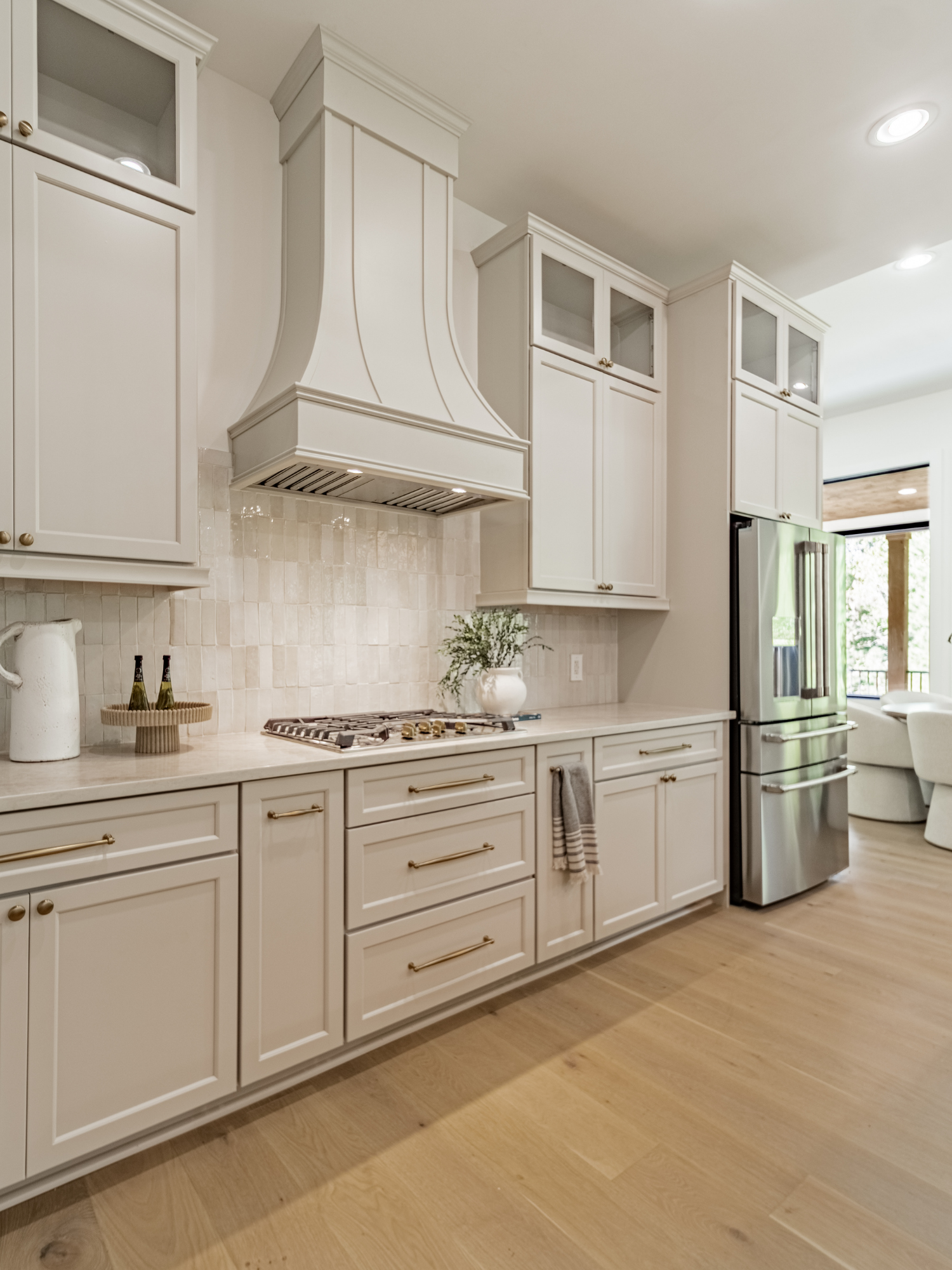 A kitchen with white cabinetry, a beige tiled backsplash, a built-in stainless steel refrigerator, and a wooden floor.