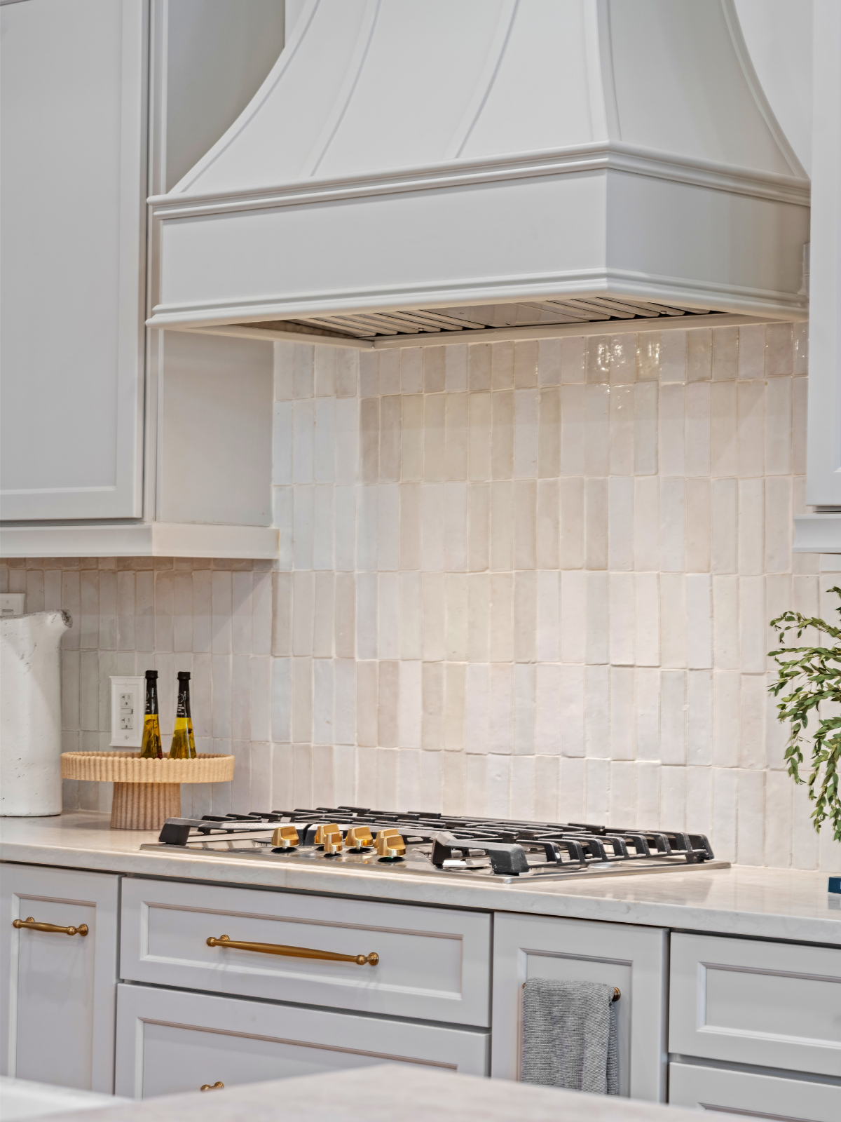 White kitchen with beige tiled backsplash, white cabinets, and a gas stove with gold knobs.