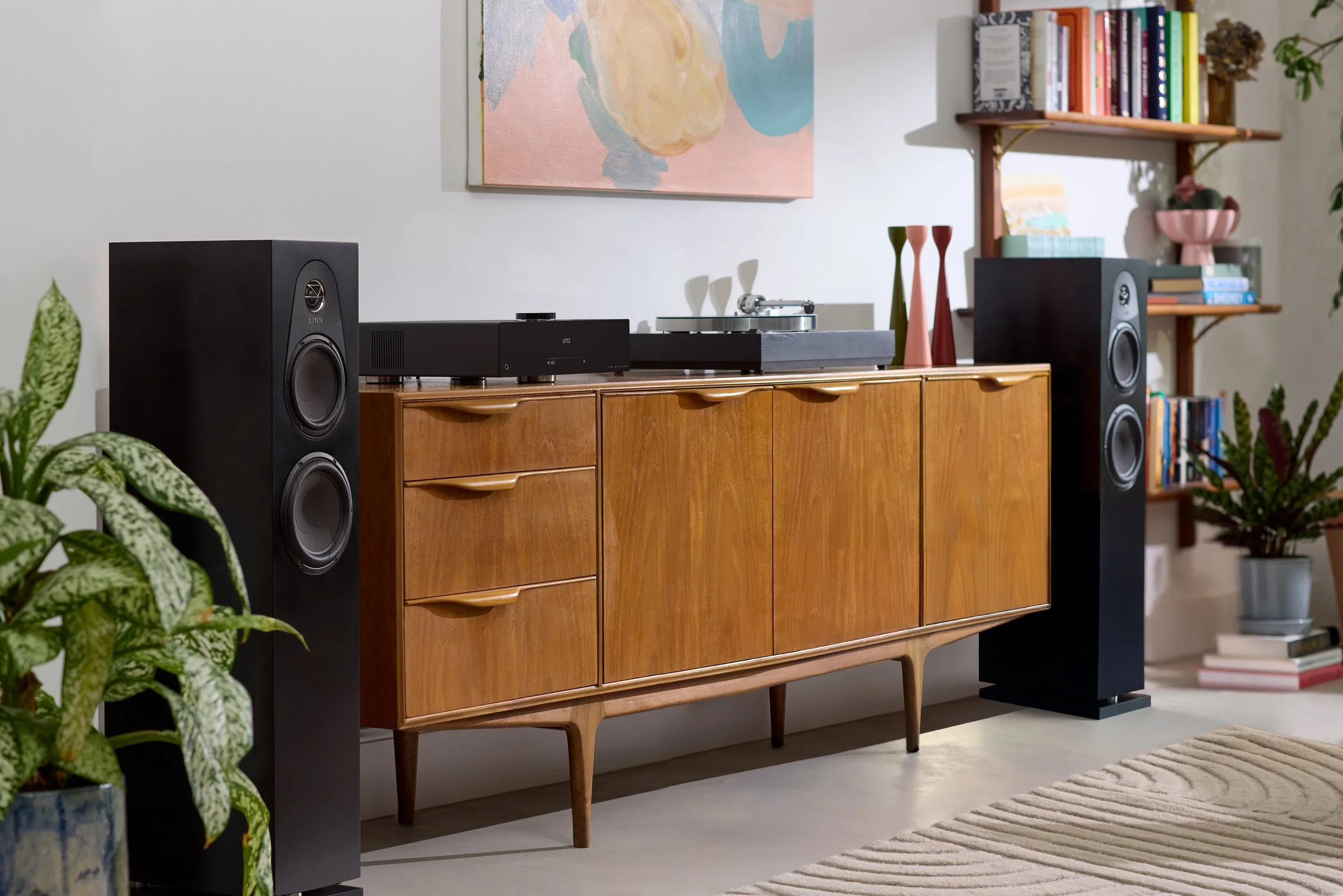 Soggiorno con mobile in legno, stereo Linn con due altoparlanti neri, scaffale con libri colorati, piante e decorazioni