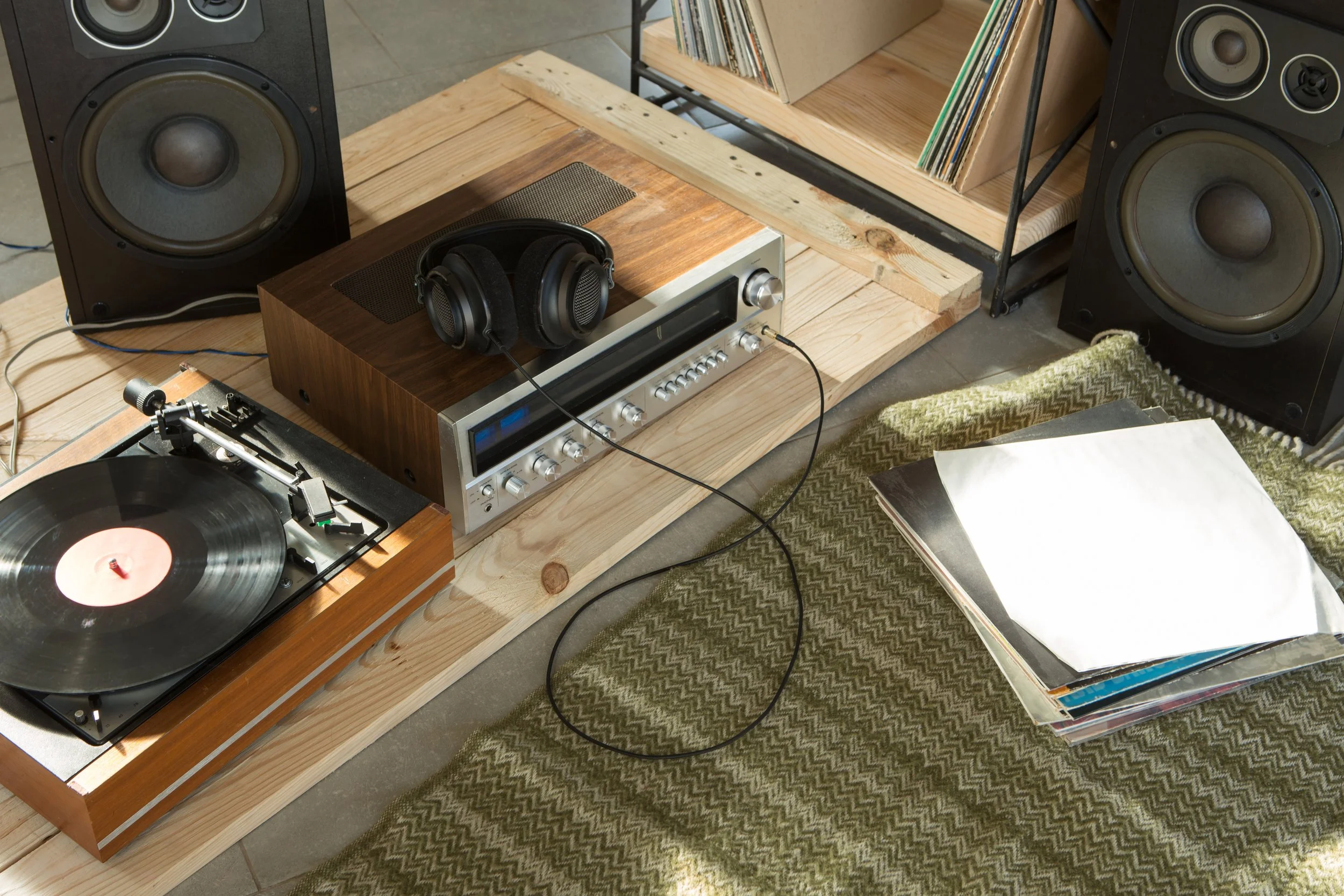 Configurazione di un sistema audio con diffusori grandi, un amplificatore con cuffie posizionate sopra, un giradischi con vinile, e una libreria di dischi in vinile, tutto su un tavolo di legno in un ambiente domestico.