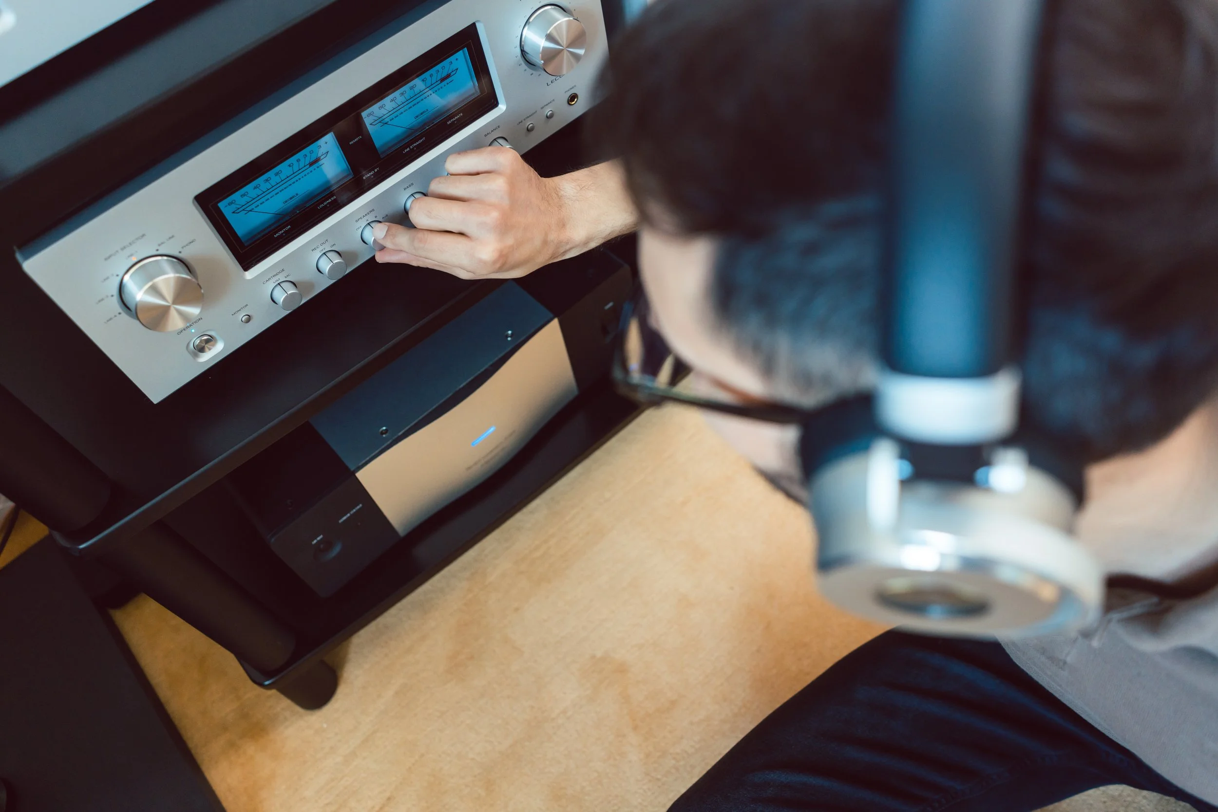 Una persona sta regolando un amplificatore stereo con due altoparlanti, visibile solo parte del corpo e del microfono al centro dell'immagine.