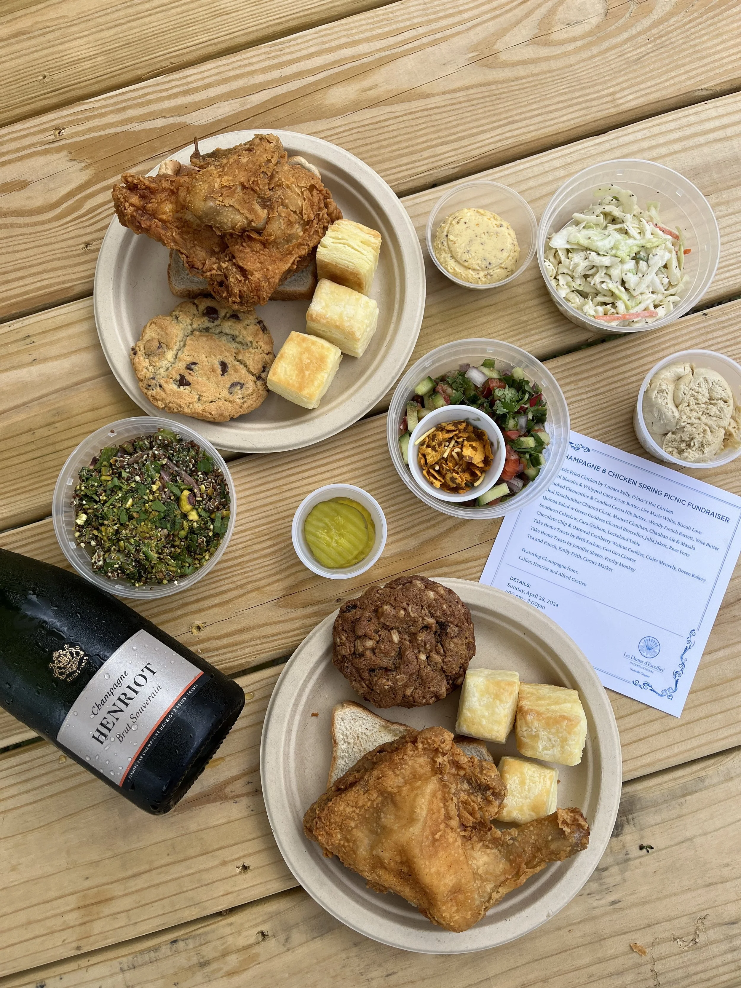  A top-down table scape of platters of fried chicken and biscuits on paper plates with sides of salads and coleslaw from a Les Dames Nashville event 