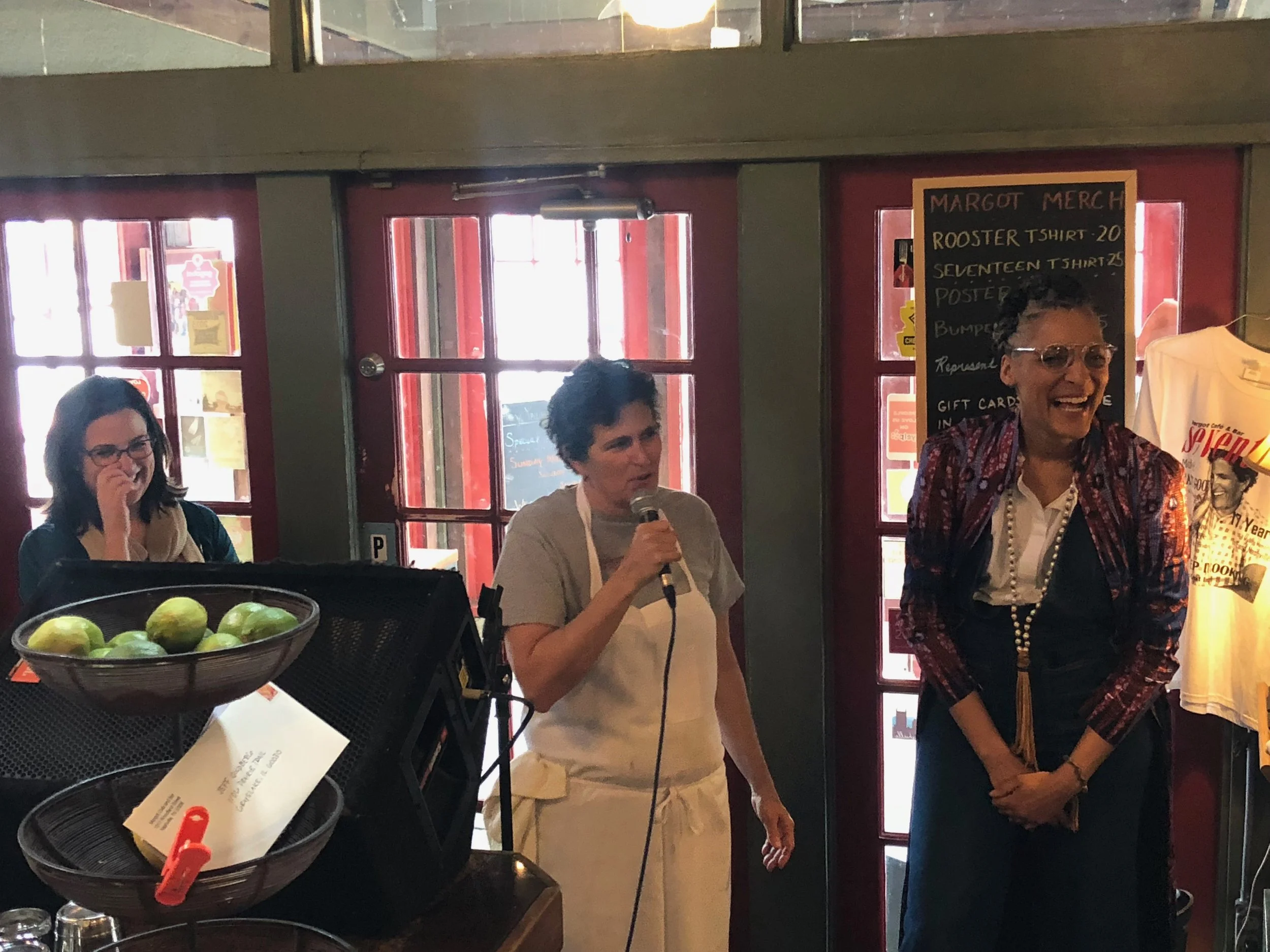  Chef Margot McCormack speaking while celebrity chef Carla Hall stands by her laughing as they speak to a room of women at a Les Dames Nashville lunch event at Cafe Margot in Nashville, TN 