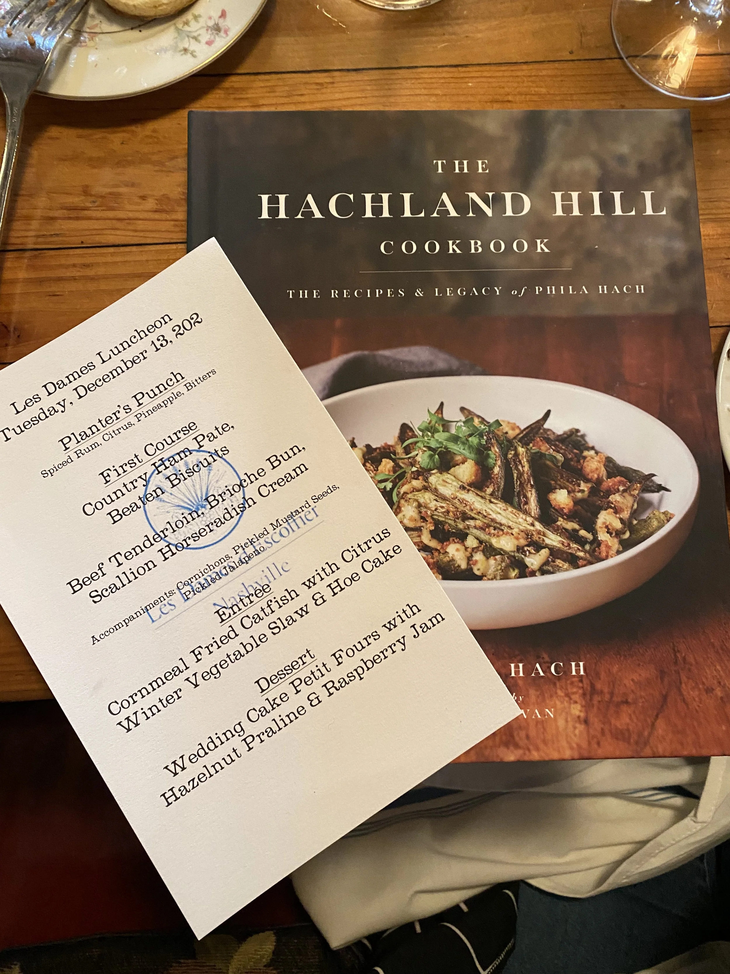  A picture of a menu sitting on top of the book The Hachland Hill Cookbook as part of a Les Dames Nashville lunch event at Cafe Margot in Nashville, TN 