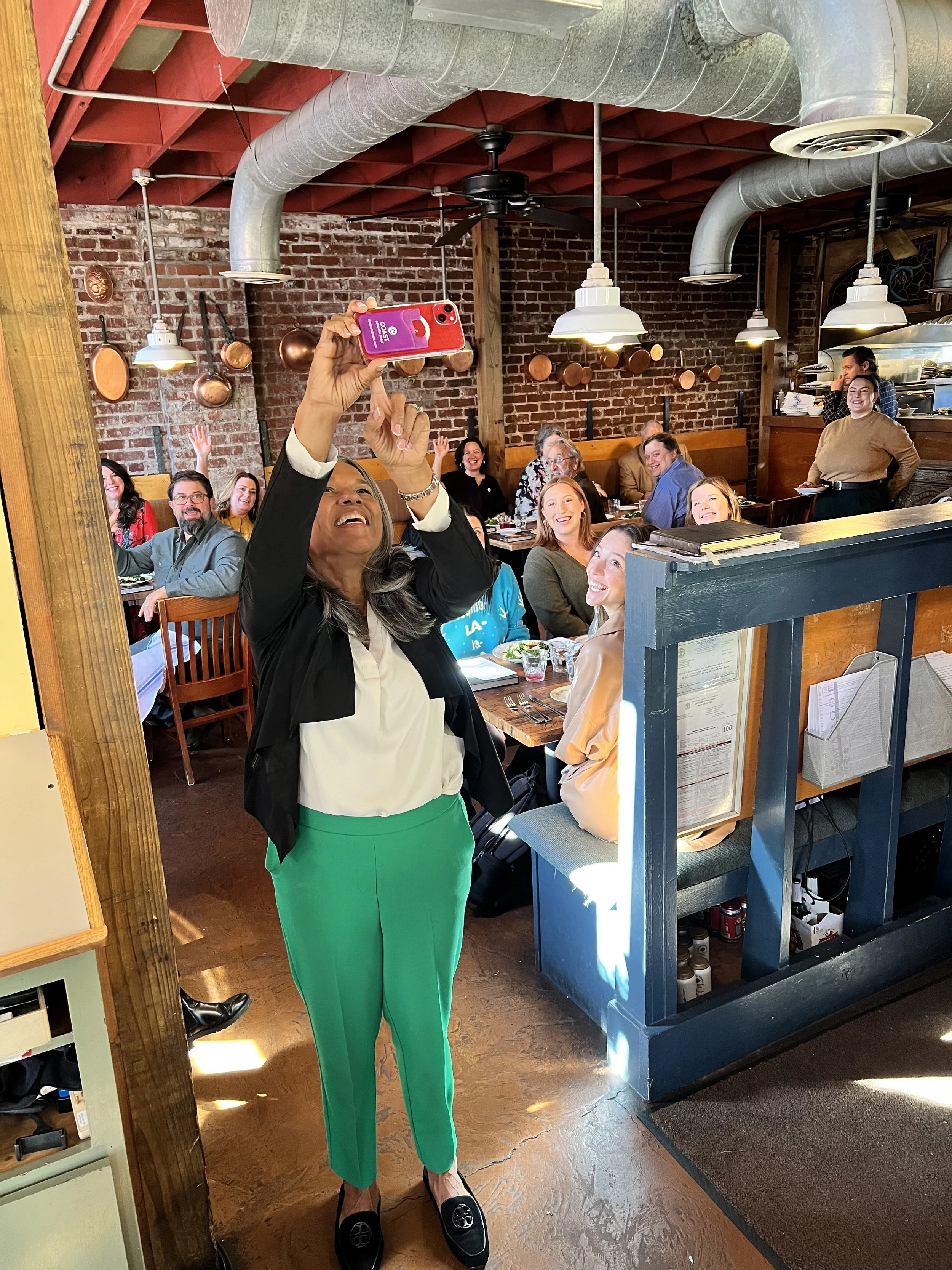  Chef and author Toni Tipton Martin holding up her phone to take a selfie with women behind her a Les Dames Nashville lunch event at Cafe Margot in Nashville, TN 