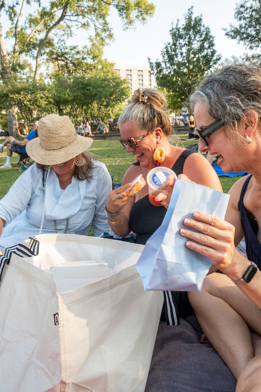 Three women sitting at a park sharing a tote bag of food at a les dames nashville picnic event
