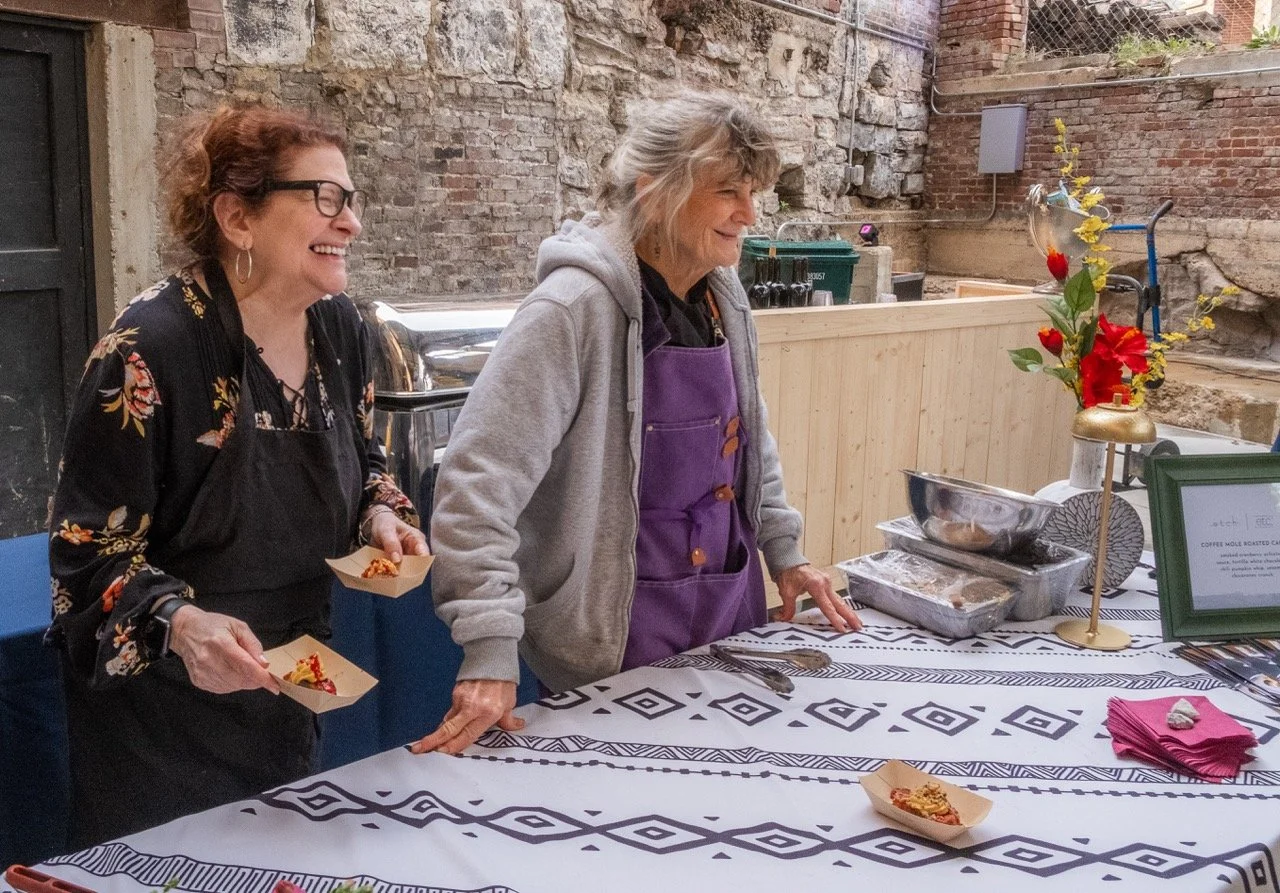 Chef Deb Paquette standing at a table serving food with a volunteer at a les dames nashville event