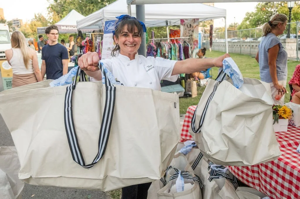 Chef Patricia Marzella holding up two canvas tote bags that hold picnic lunches at a fundraiser for les dames nashville