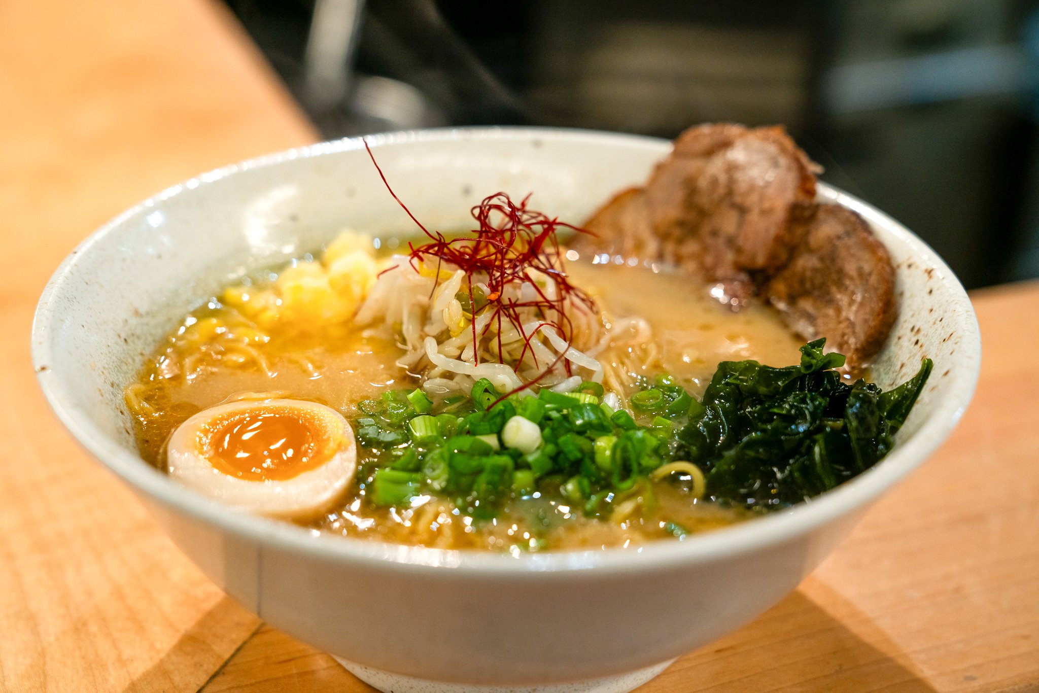 Bowl of Hokkaido-style miso ramen at Satori Ramen Bar with soft-boiled egg, shredded chashu pork, green onions, nori seaweed, bean sprouts, and red chili threads.