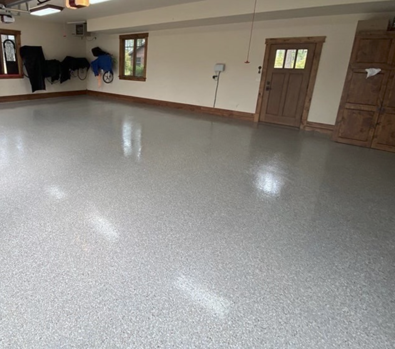 Empty garage with a polished epoxy floor, wooden trim, and windows.