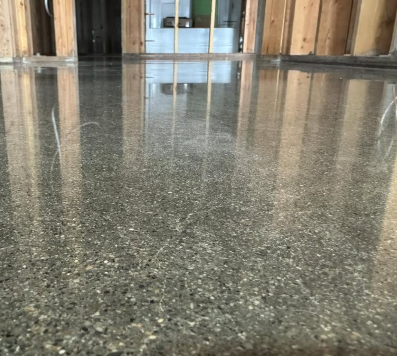 Newly poured concrete floor in an unfinished room with wooden framing and a window in the background.