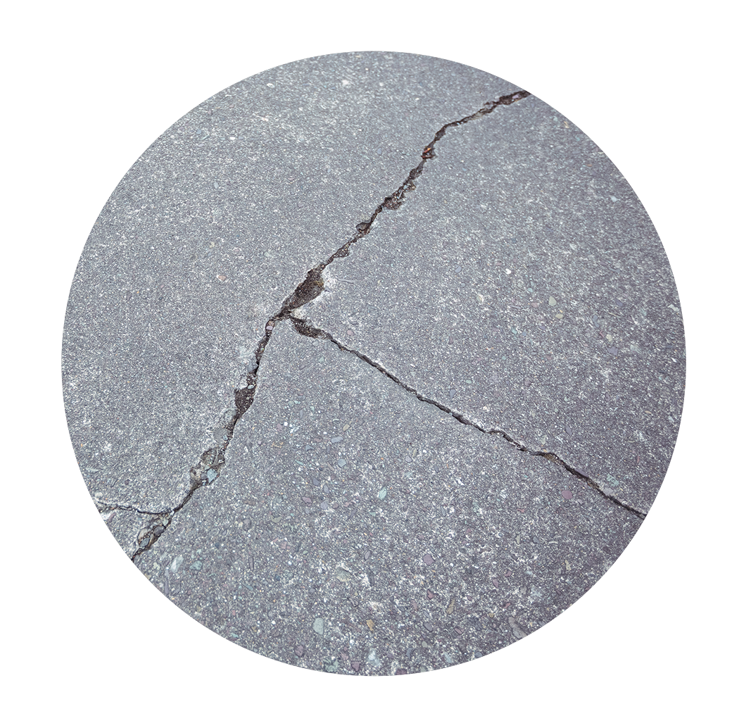 Close-up of a cracked concrete surface with visible cracks and small pebbles embedded, surrounded by a cracked concrete background.