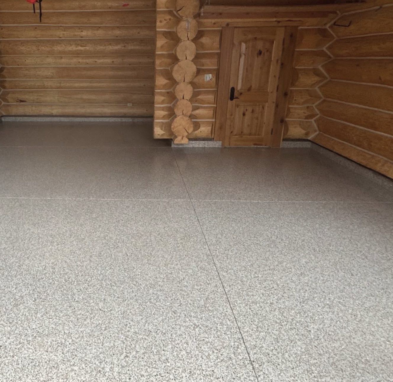 Interior of a room with wooden log walls and a beige tiled floor, featuring a wooden door in the corner.