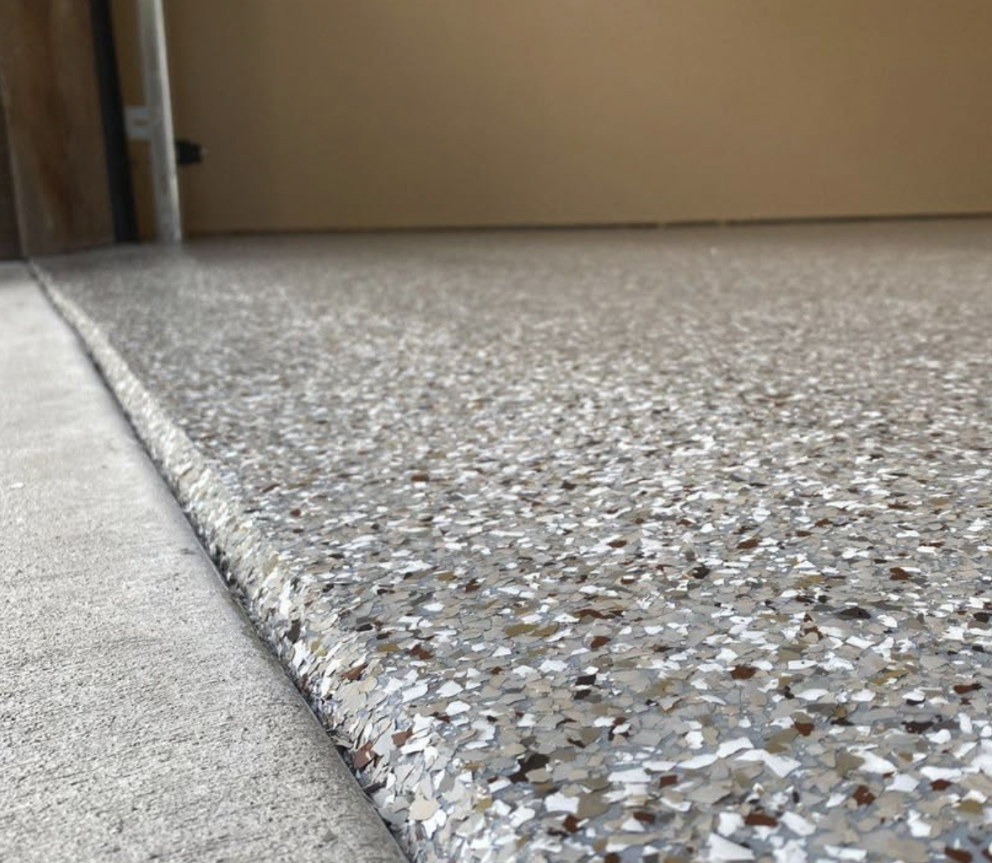 Close-up of a polished terrazzo floor with a concrete sidewalk curb and a beige wall in the background.