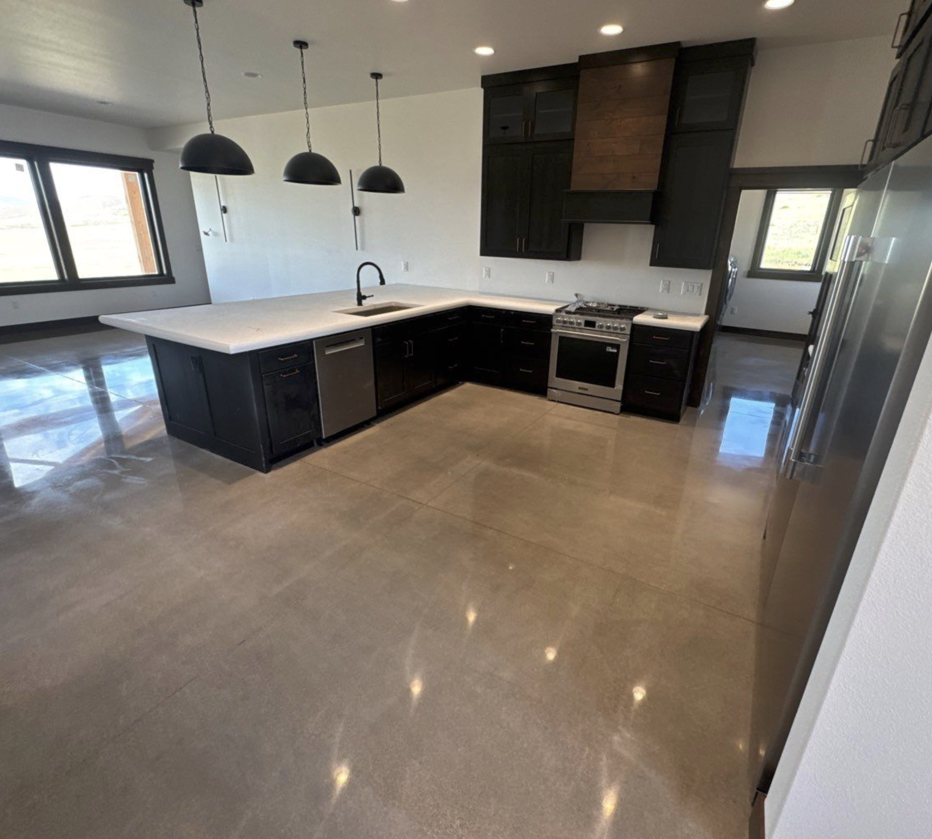 Modern kitchen with black cabinets, white countertops, stainless steel appliances, pendant lights, and large windows with a view outside.