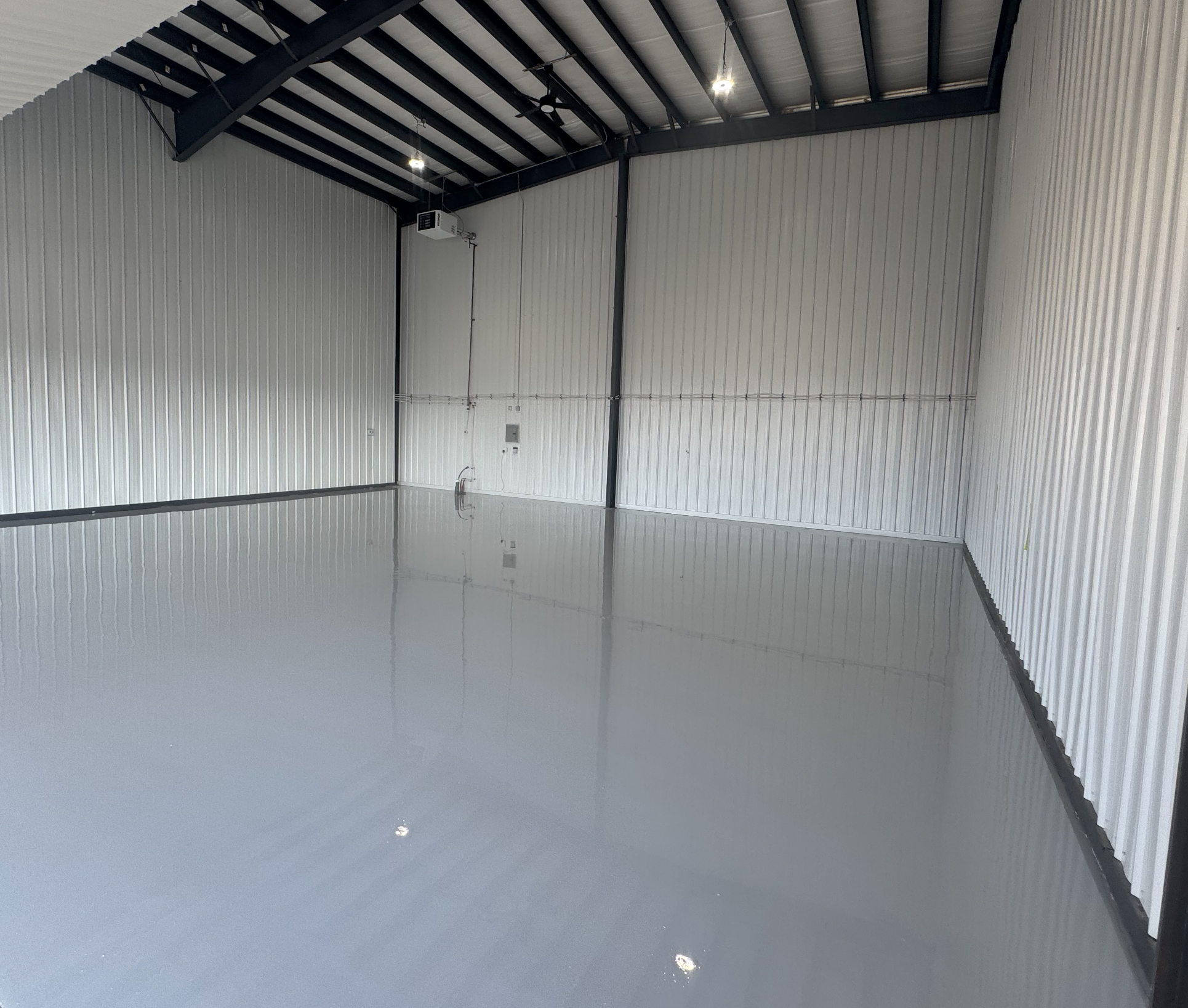 Empty indoor warehouse or industrial space with shiny polished concrete floor, metal wall panels, and overhead lighting.