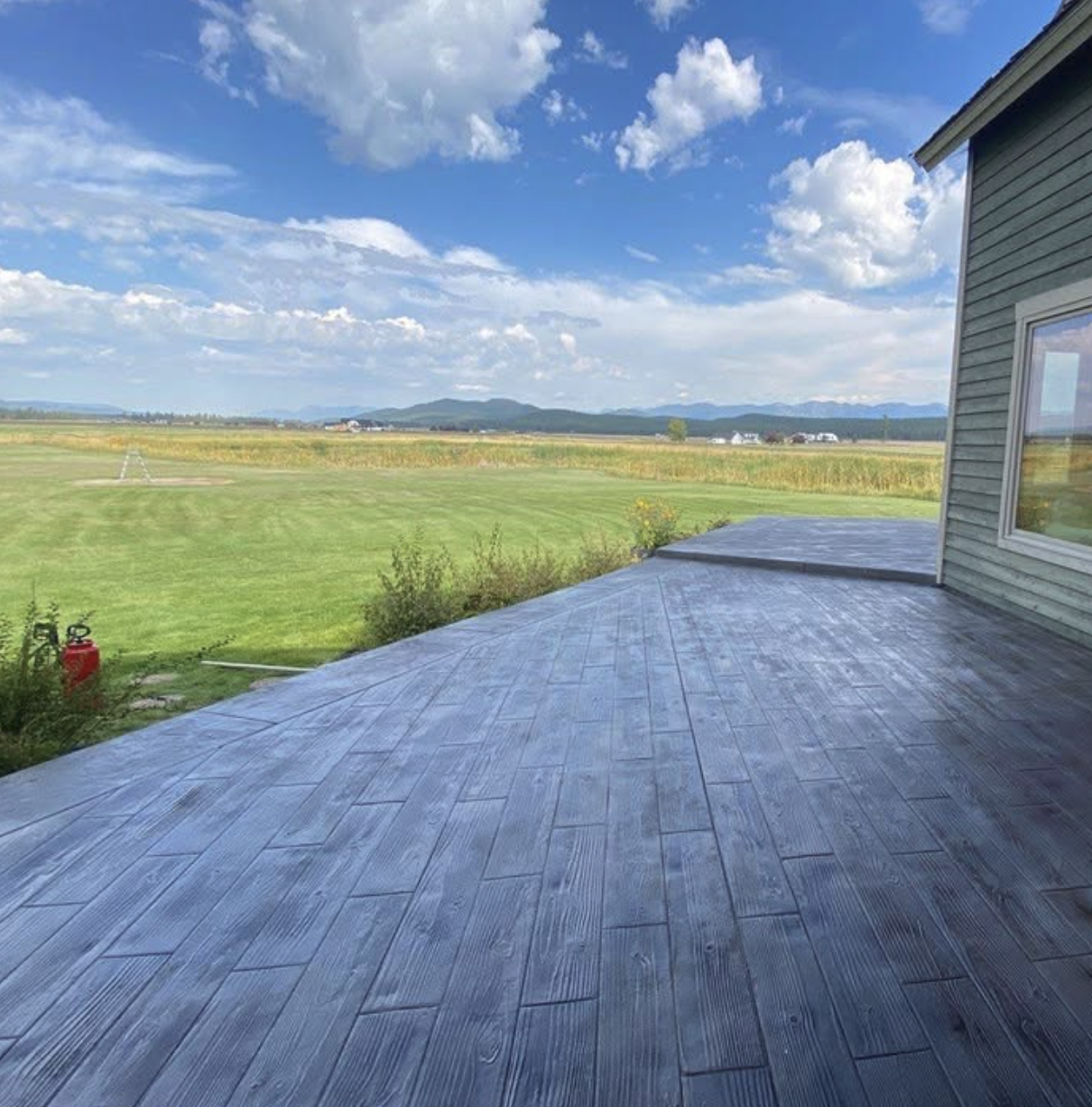 View of a backyard deck overlooking a green grassy field with mountains in the distance under a partly cloudy sky.