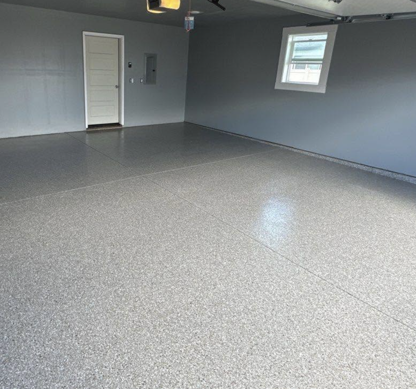 Empty garage with speckled epoxy floor, gray painted walls, a white door, a small window, and electrical panels.