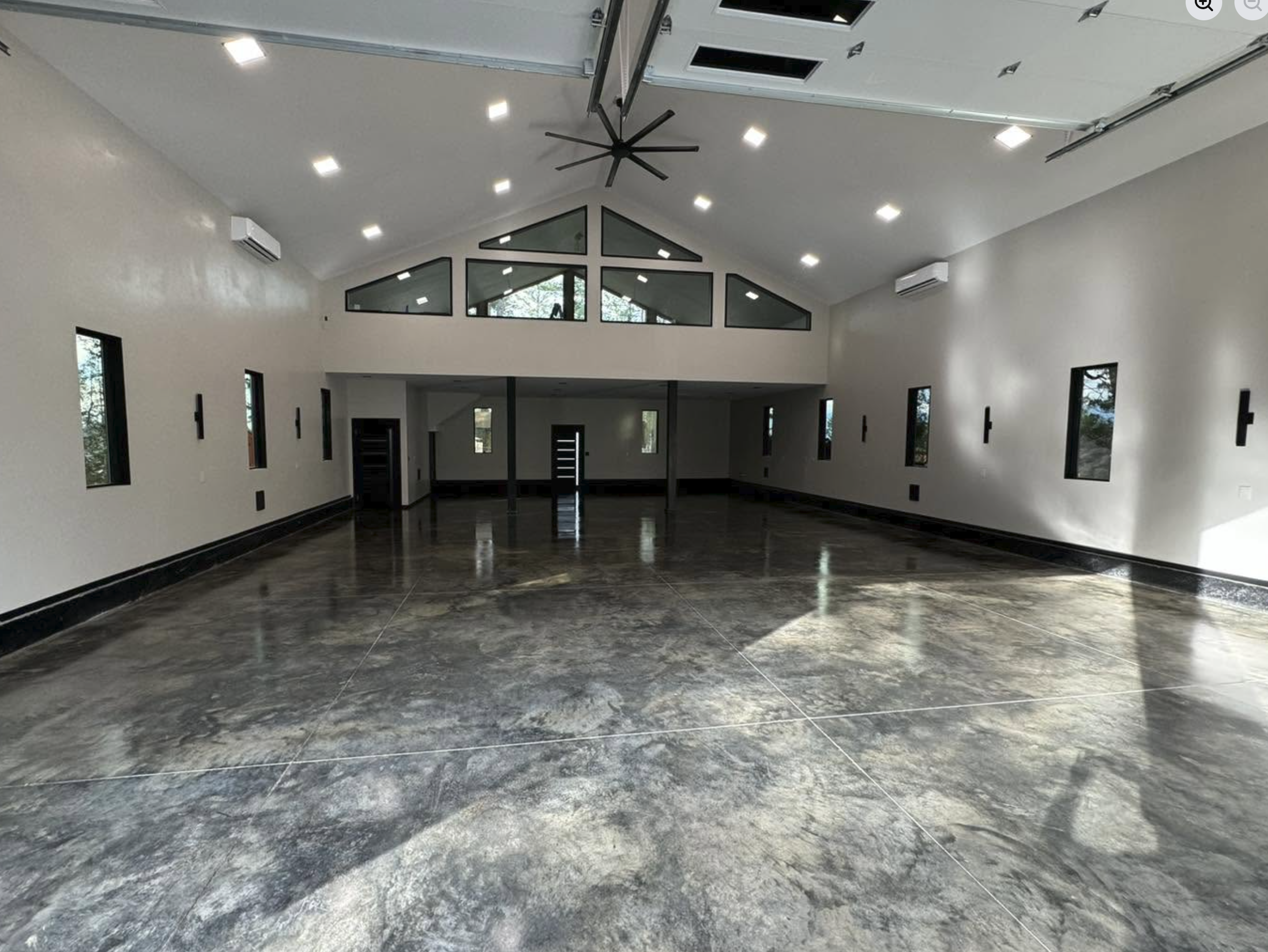 Modern large indoor space with dark marble flooring, white walls, black accents, high vaulted ceiling with recessed lighting, triangular window design at the front, and multiple small rectangular windows on the sides.