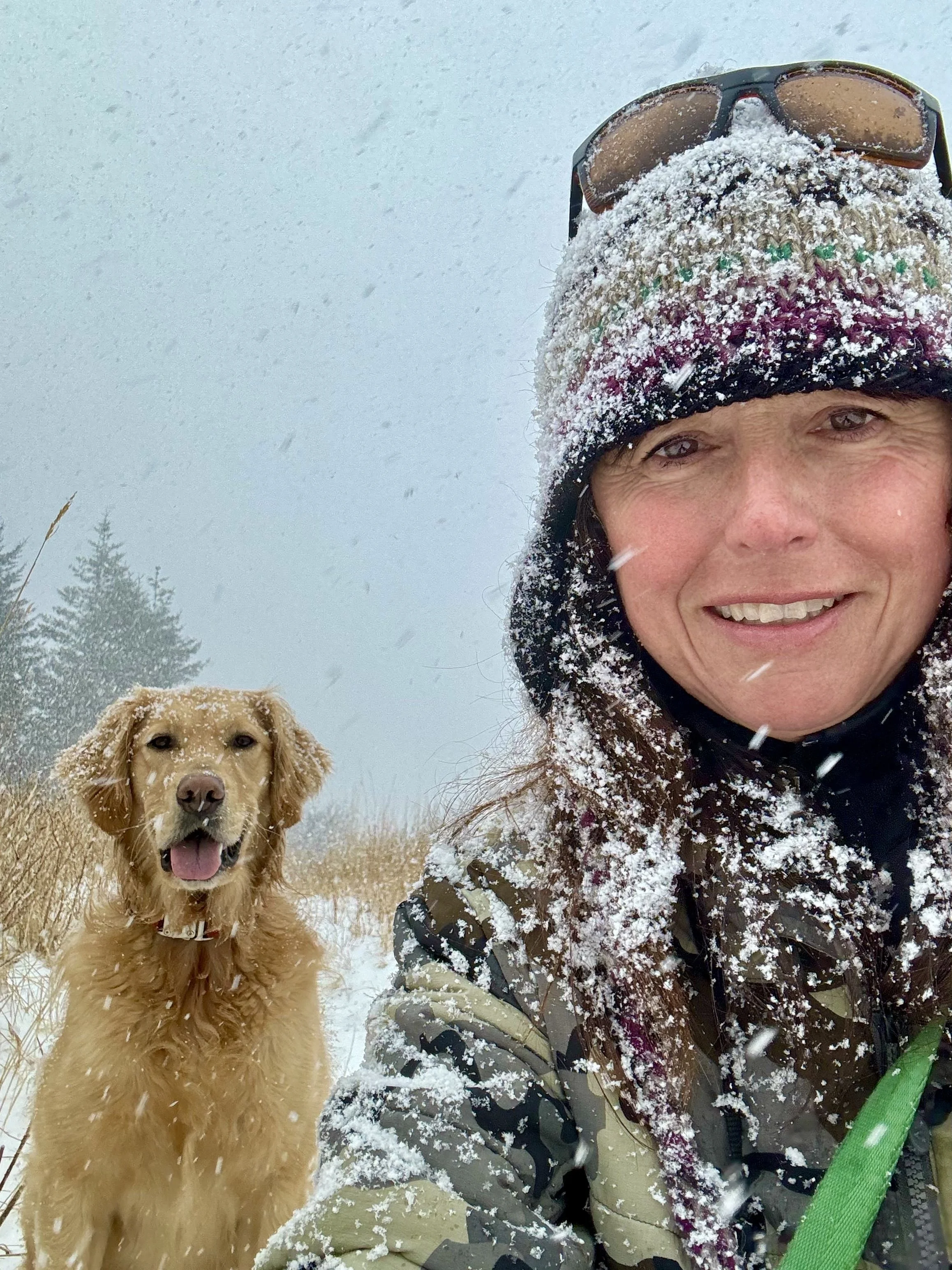Jennifer Smith outdoors in falling snow with her golden retriever