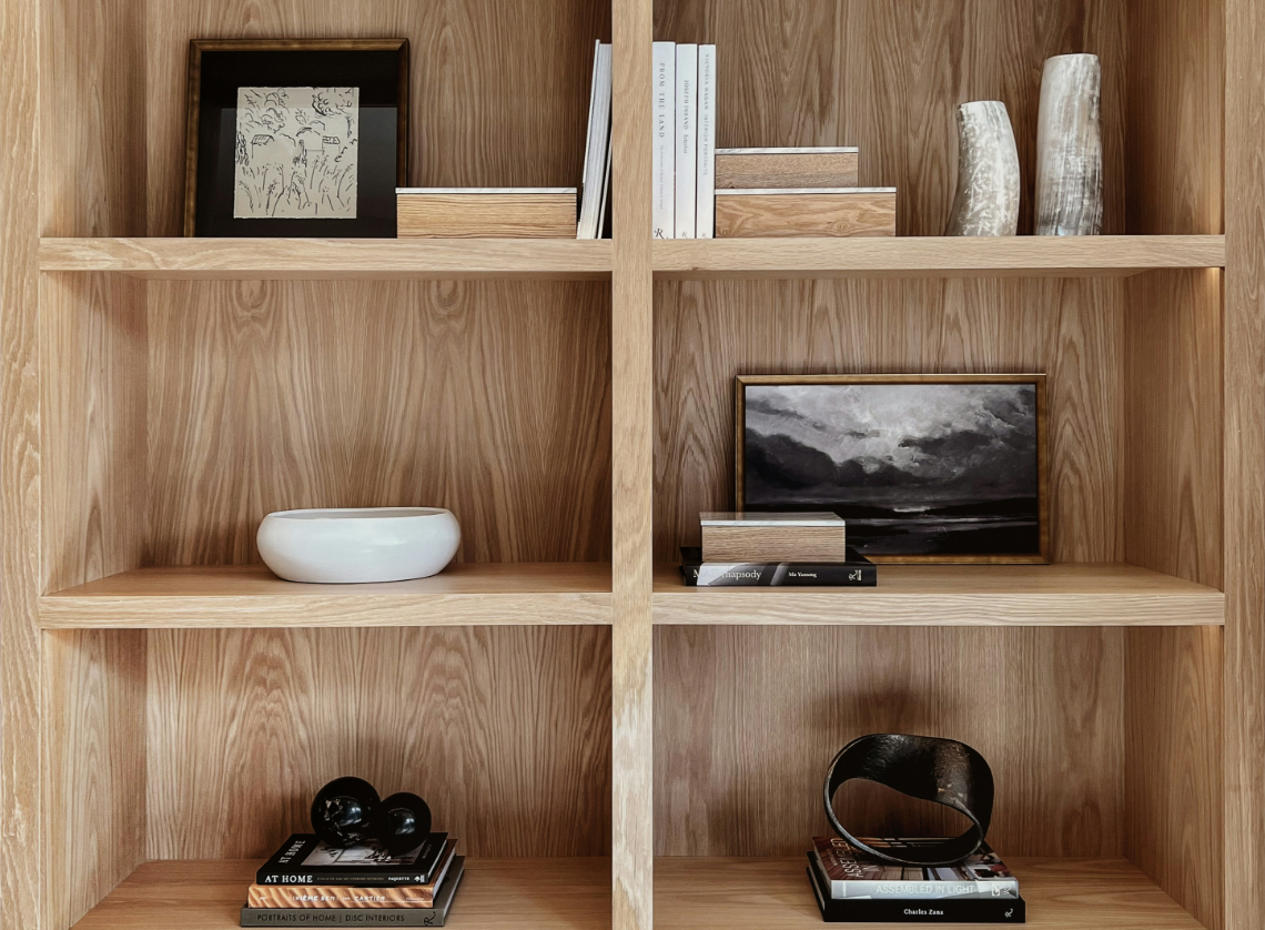 Wooden bookshelf with various decorative items and books, including framed artwork, vases, a white bowl, black spheres, and a black and gold sculpture.
