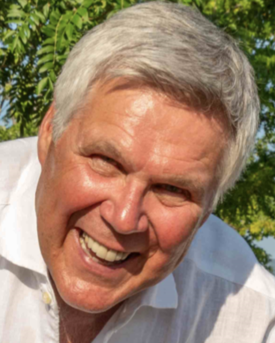 Close-up of Robin Jacobsen smiling outdoors with green trees in the background.