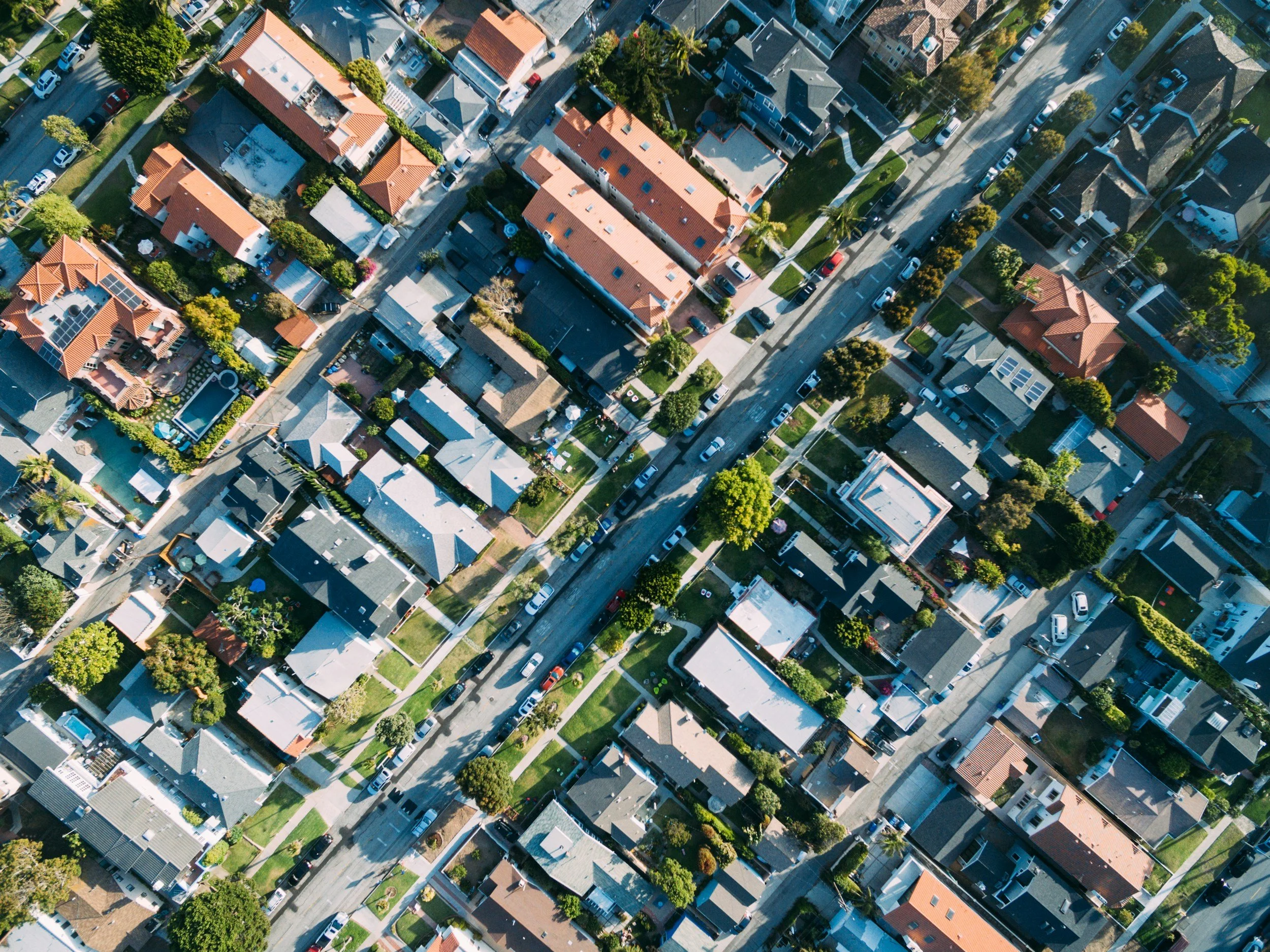 An aerial view of a residential neighborhood with houses, trees, roads, and parked cars.