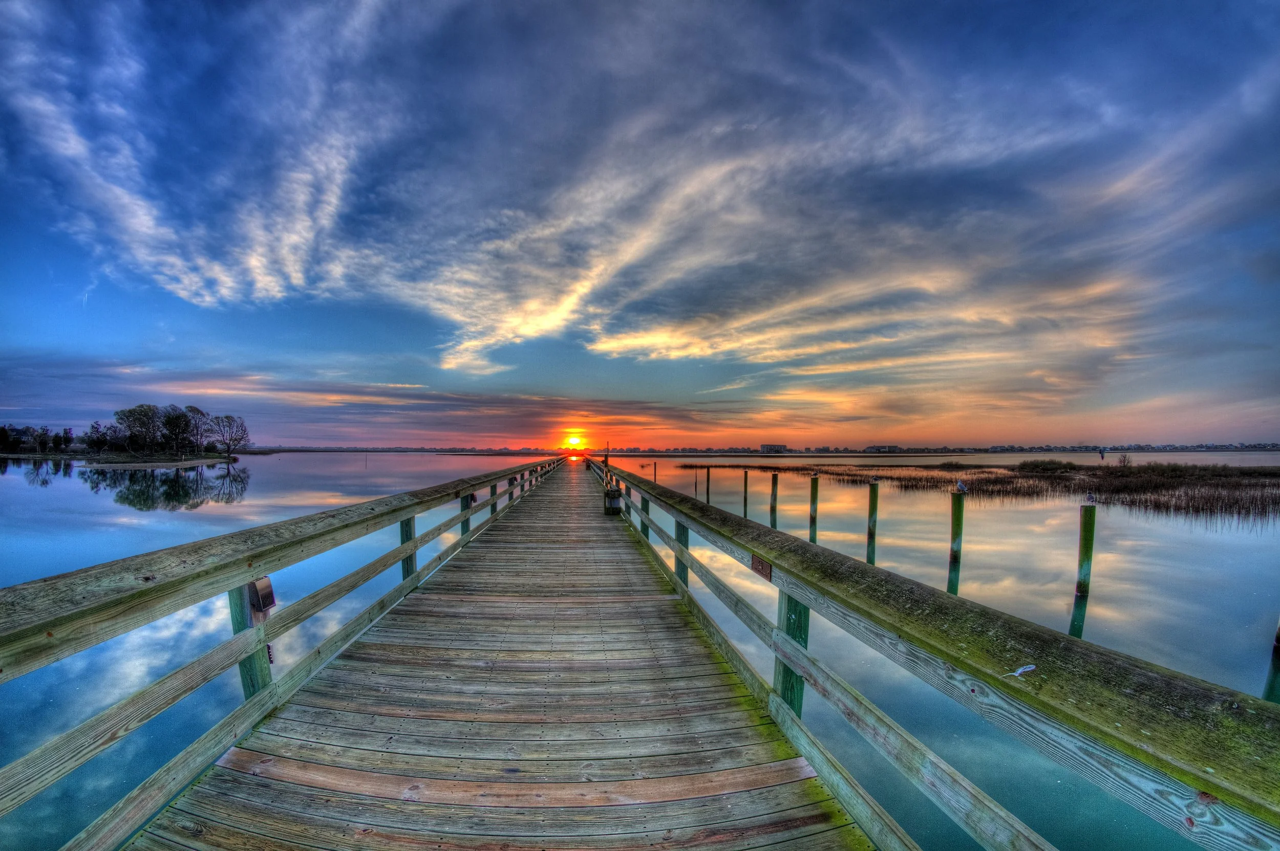 Sunset over a calm lake with a wooden pier extending into the water, surrounded by trees and reflections of the sky in the water in Pawleys Island South Carolina