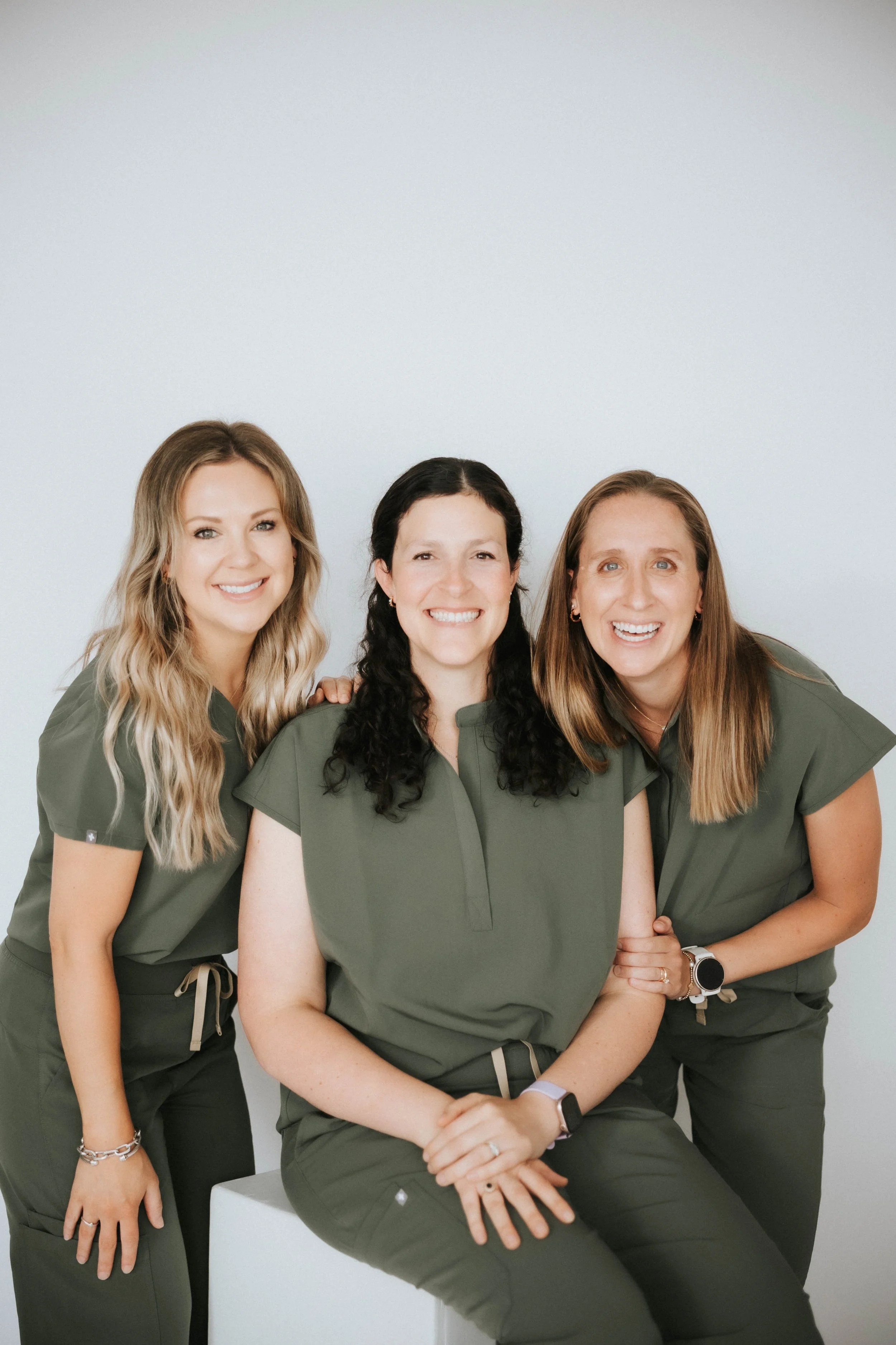 Group of four women in matching green work uniforms smiling and posing together against a plain white background.