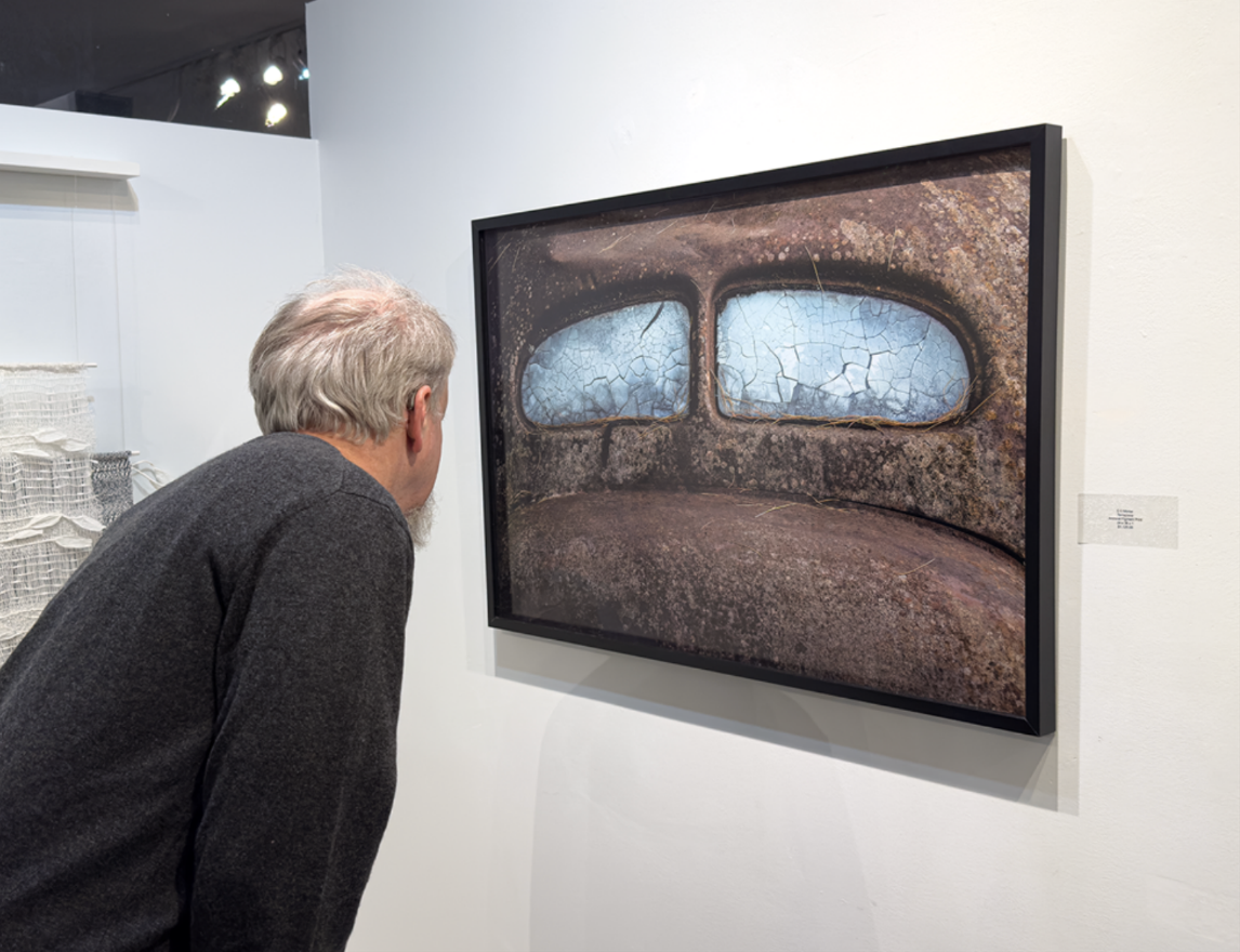 A man looking at an abstract art piece featuring two cracked, blue-tinted windows on a rusted surface.