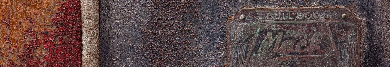 Close-up of a weathered metal sign for Mack, a bulldog breed, with rust and peeling paint.