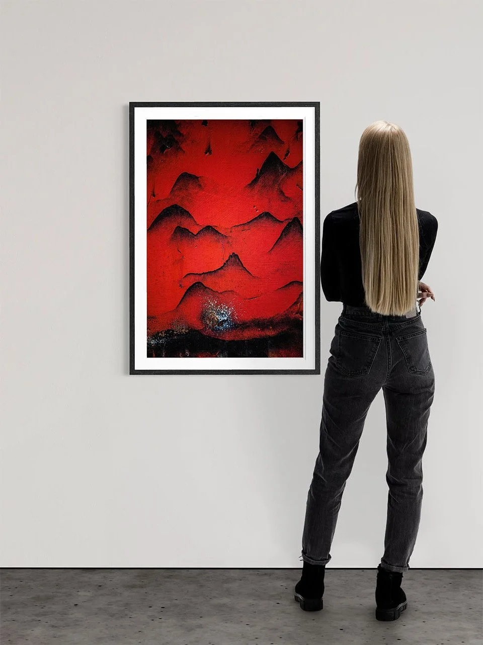 A woman with long blonde hair wearing a black top and black jeans stands with her back to the camera, observing a red and black abstract painting in a gallery.
