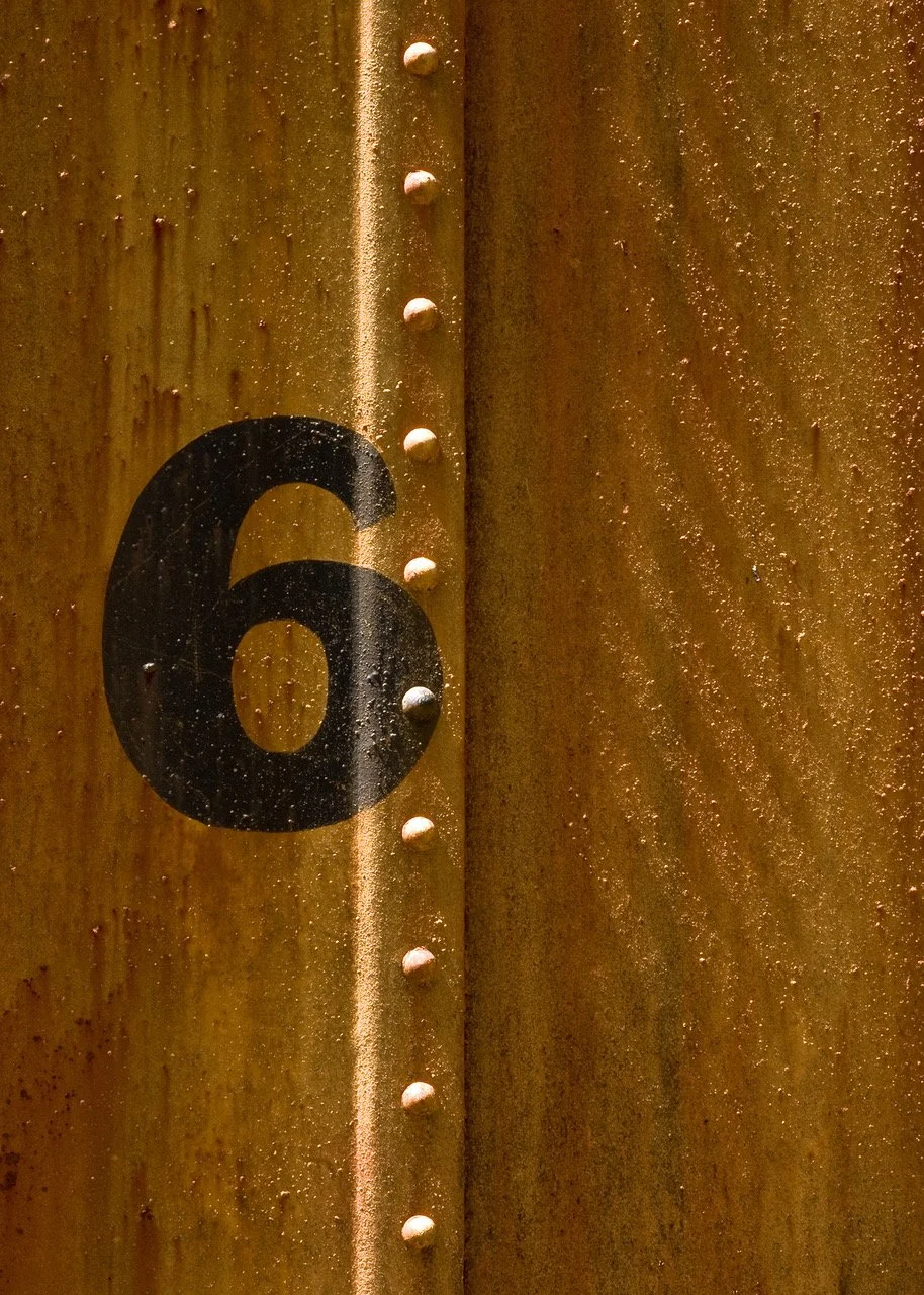 Close-up of a rusty metal surface with the number 6 painted in black, and visible rivets along a seam.
